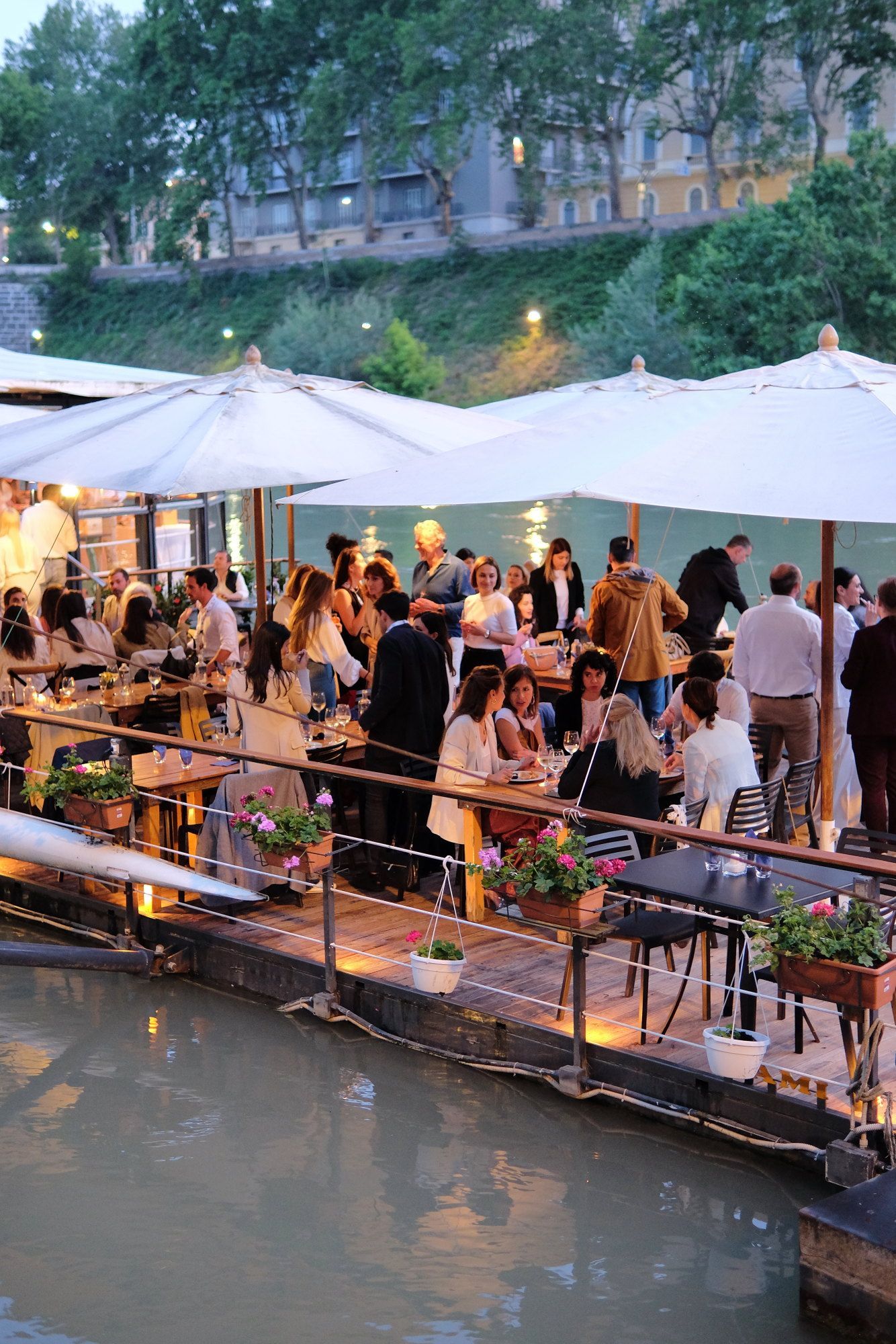 Un gruppo di persone è seduto a dei tavoli sotto degli ombrelloni su un molo.