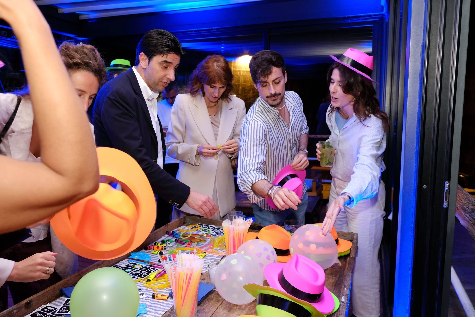 Un gruppo di persone è in piedi attorno a un tavolo con cappelli e palloncini.