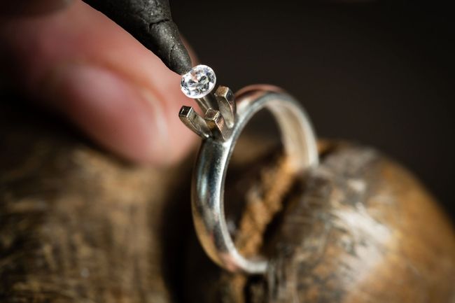 Un gioielliere che posiziona un piccolo diamante su un anello d'argento con uno strumento, primo piano.