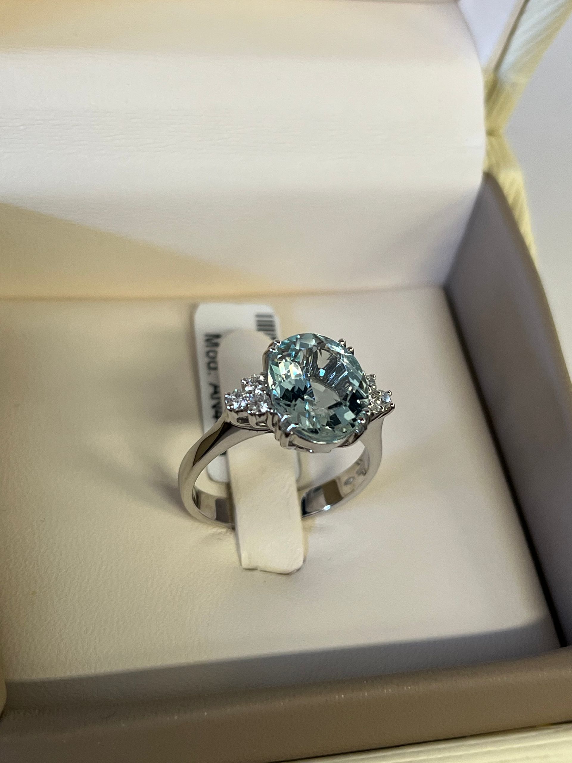 Anello in argento con pietra preziosa ovale blu e alone di diamanti, presentato in una scatola per anelli bianca.