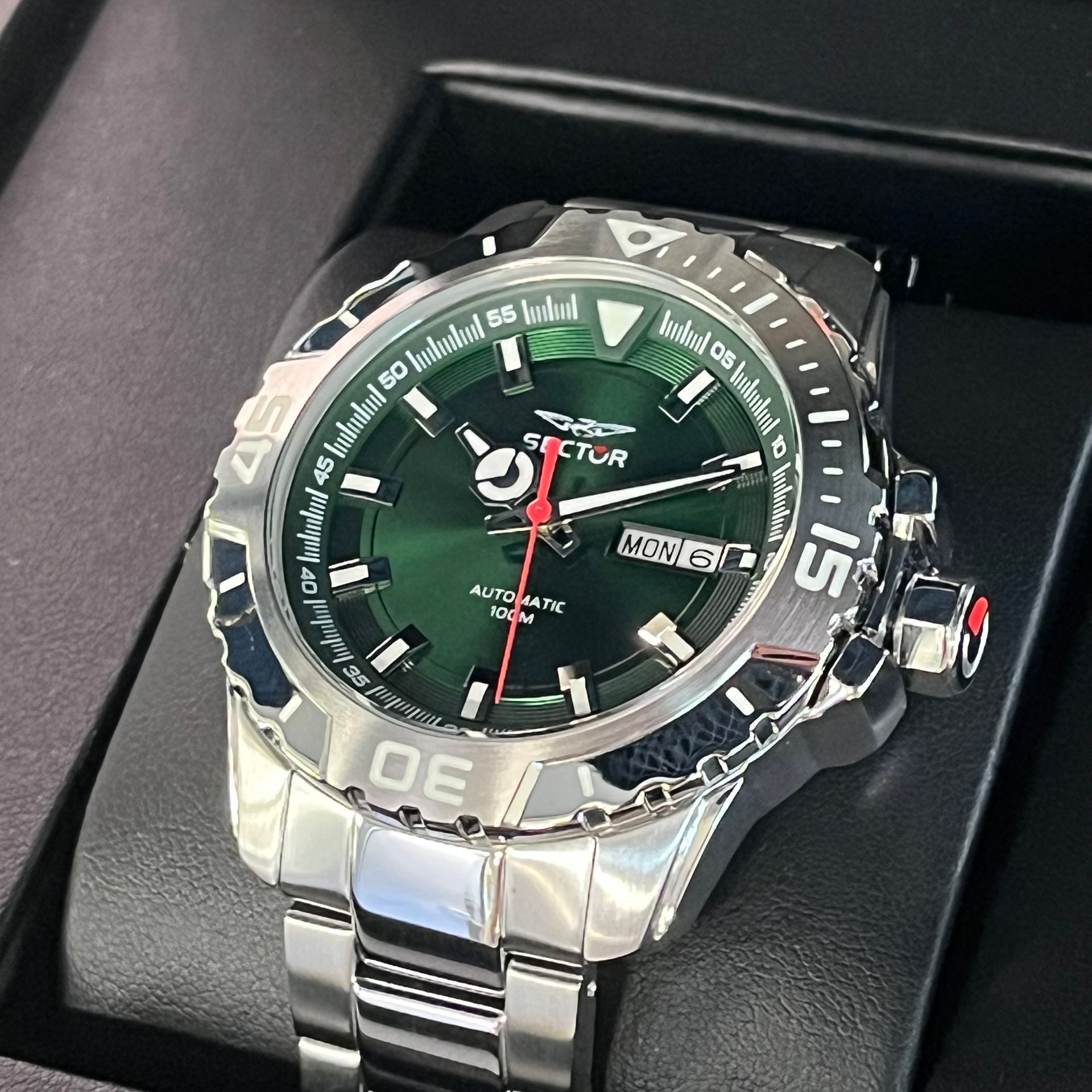 Tre orologi da polso in argento con quadrante bianco e cinturino in pelle nera o blu su una superficie verde.