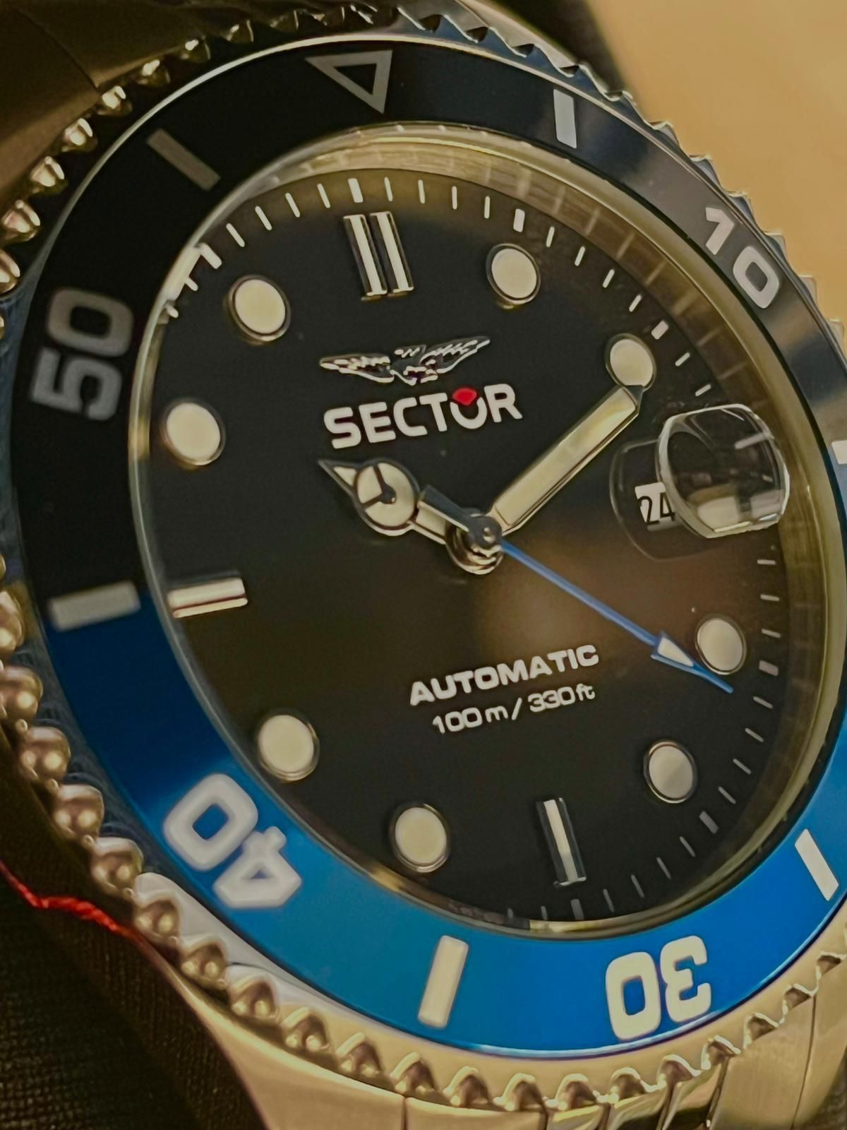 Primo piano di un orologio automatico Sector in argento con quadrante nero, lunetta blu e numeri bianchi.