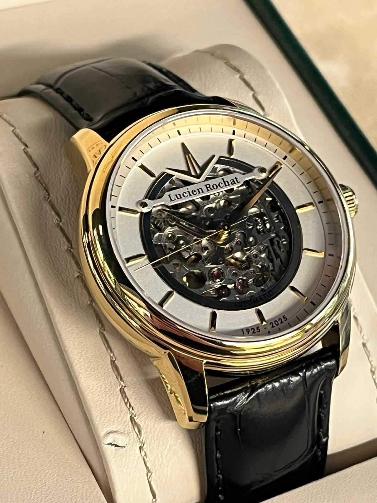 Orologio in oro con cinturino in pelle nera, quadrante scheletrato e ingranaggi visibili.