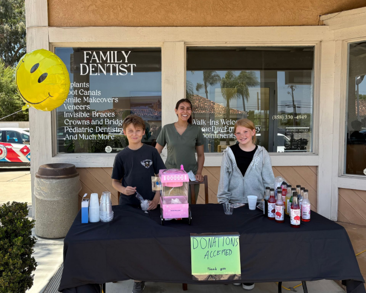 Kids at a roadside lemonade stand; selling beverages with a dental office in the background.