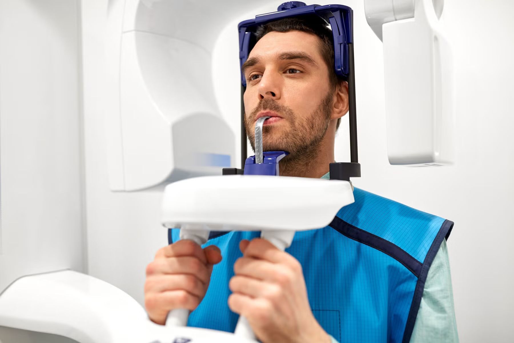 Man having dental panoramic X-ray, holding handles, wearing protective apron, in a dental office.