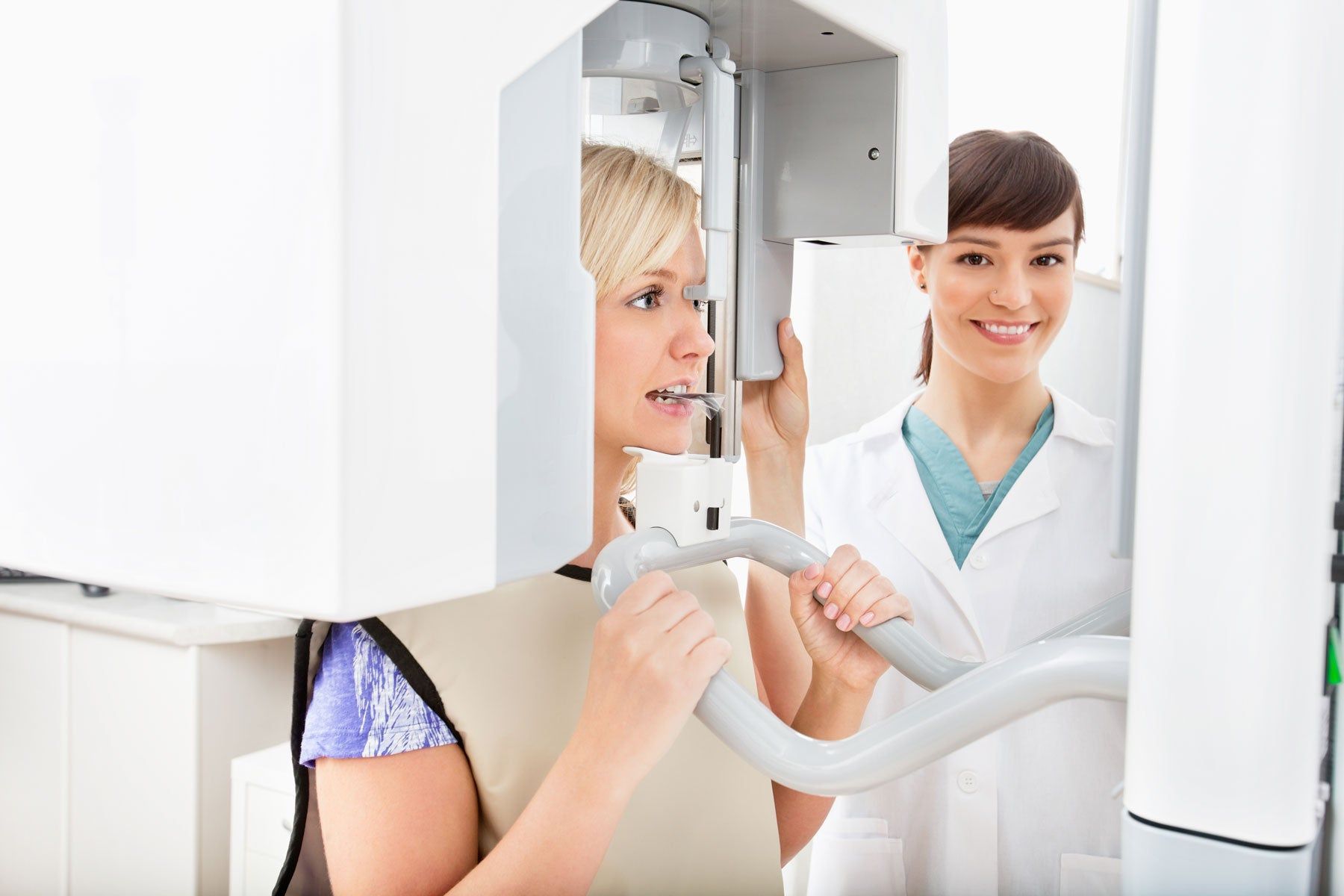 Woman in dental X-ray machine with a dentist assisting. The patient wears a protective apron.