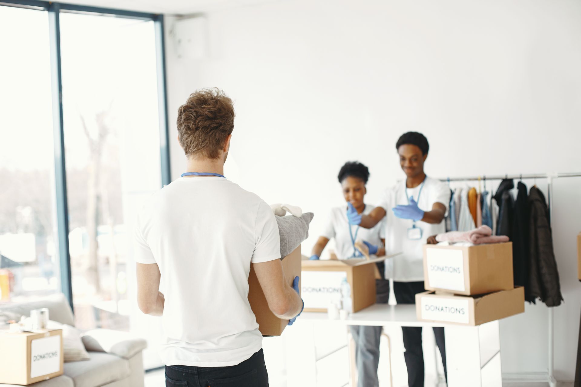 A man is carrying a box in a room while two women are standing behind him.