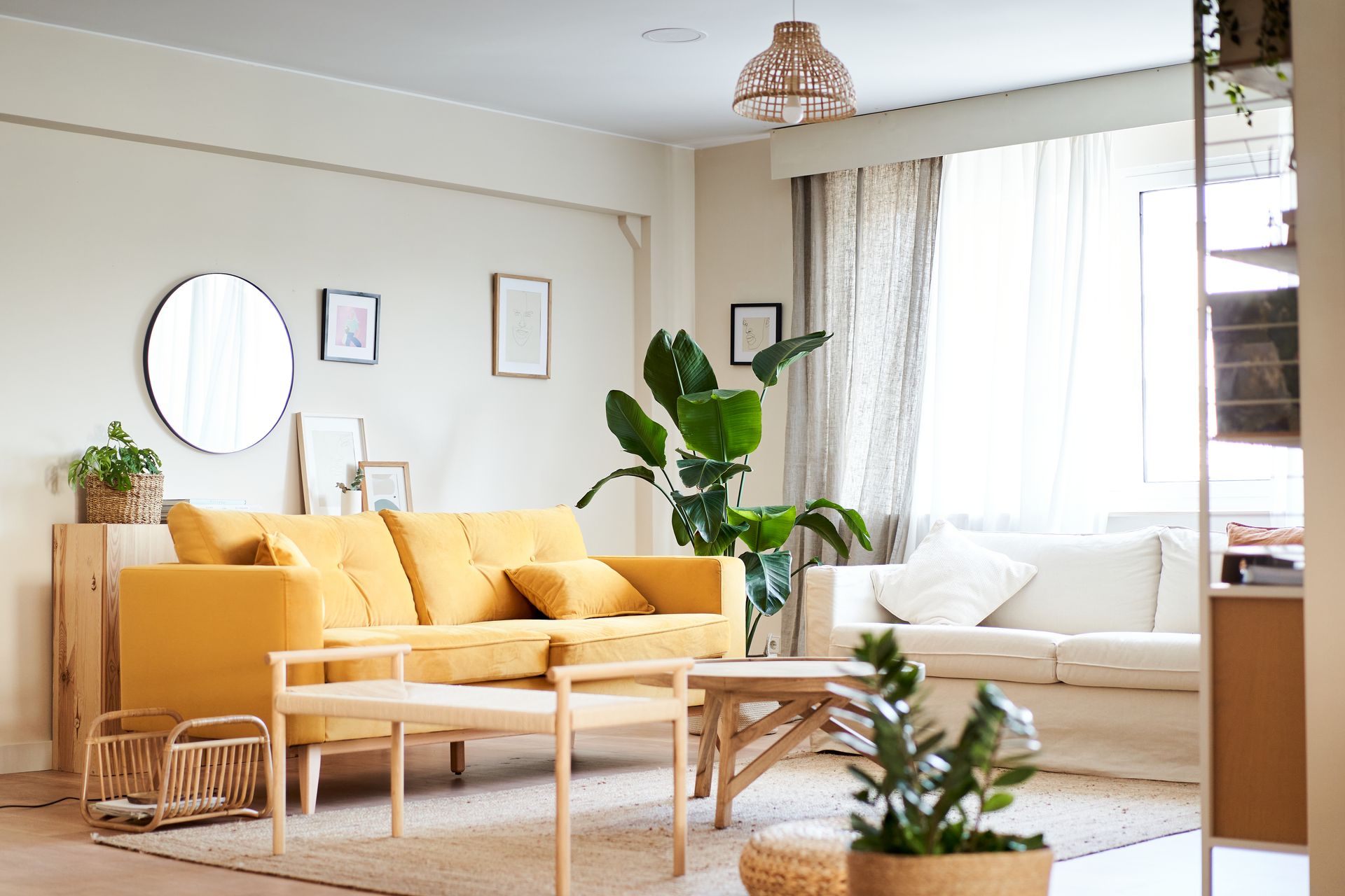 A living room with a yellow couch , white couches , a table , and a mirror.