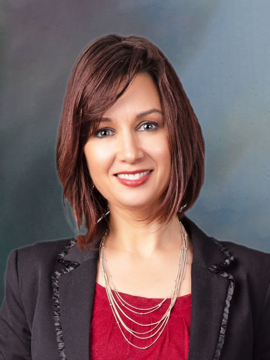 A woman wearing a red top and a black jacket smiles for the camera