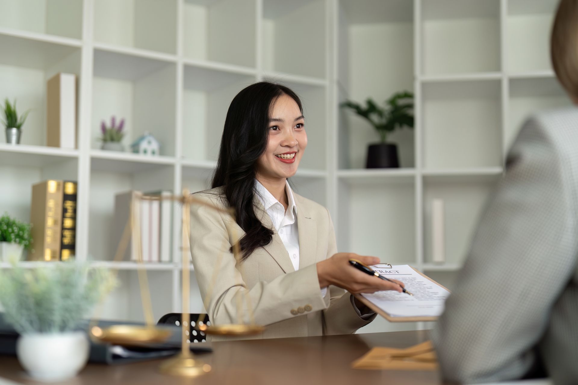 A woman is sitting at a table holding a piece of paper and talking to another woman.
