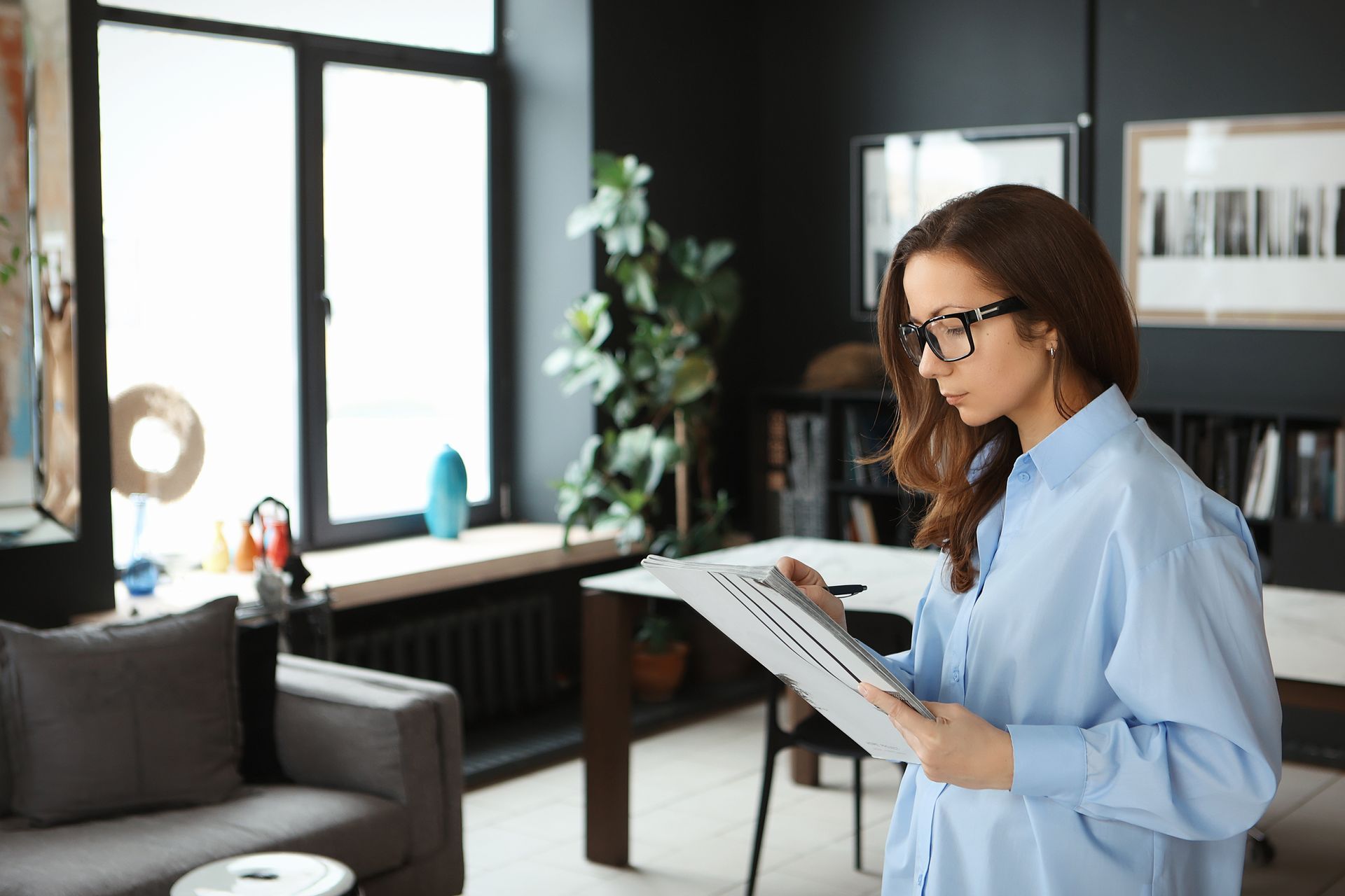 A woman is standing in a living room looking at a piece of paper.