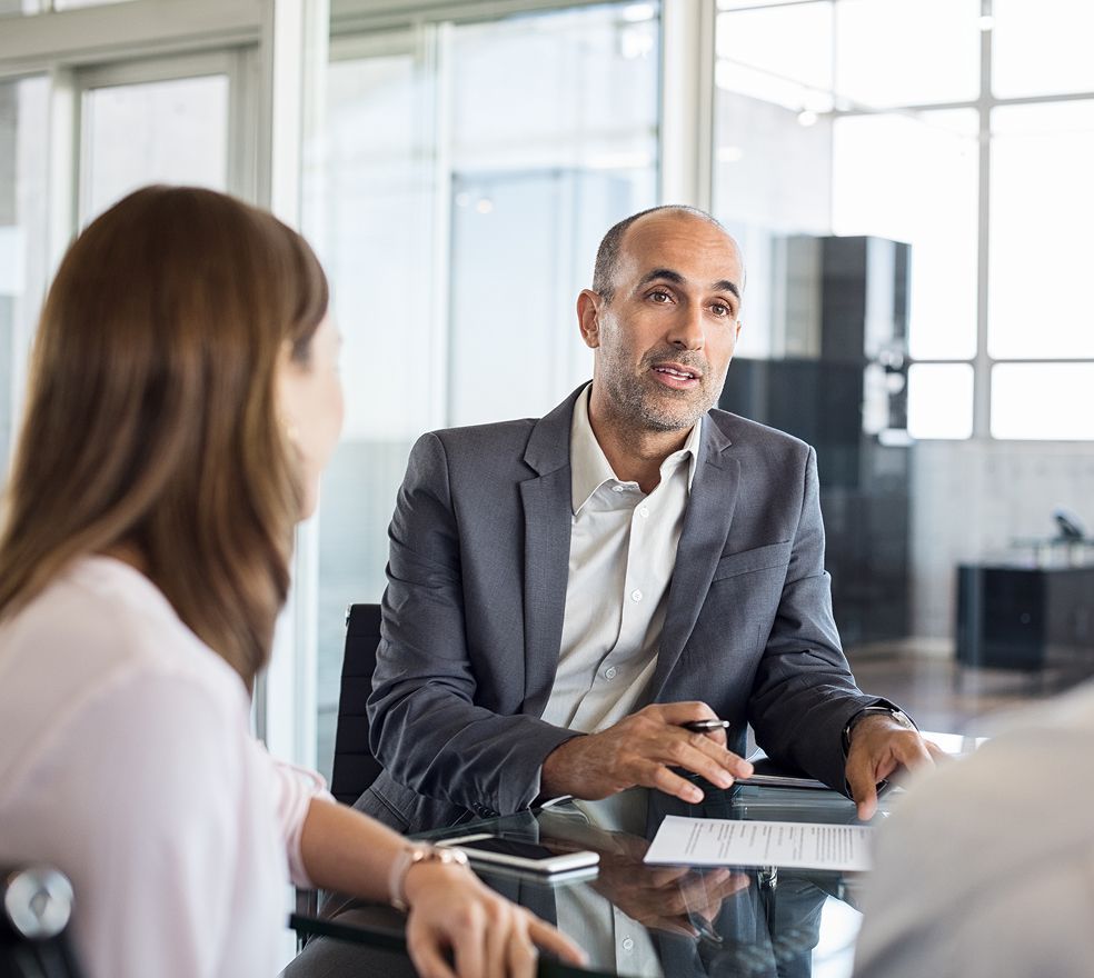 A man in a suit is sitting at a table talking to a woman.
