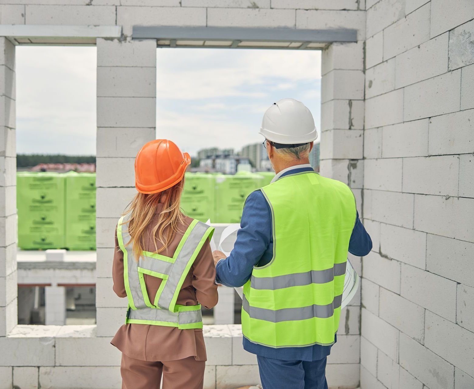 A man and a woman are looking out of a window at a construction site.