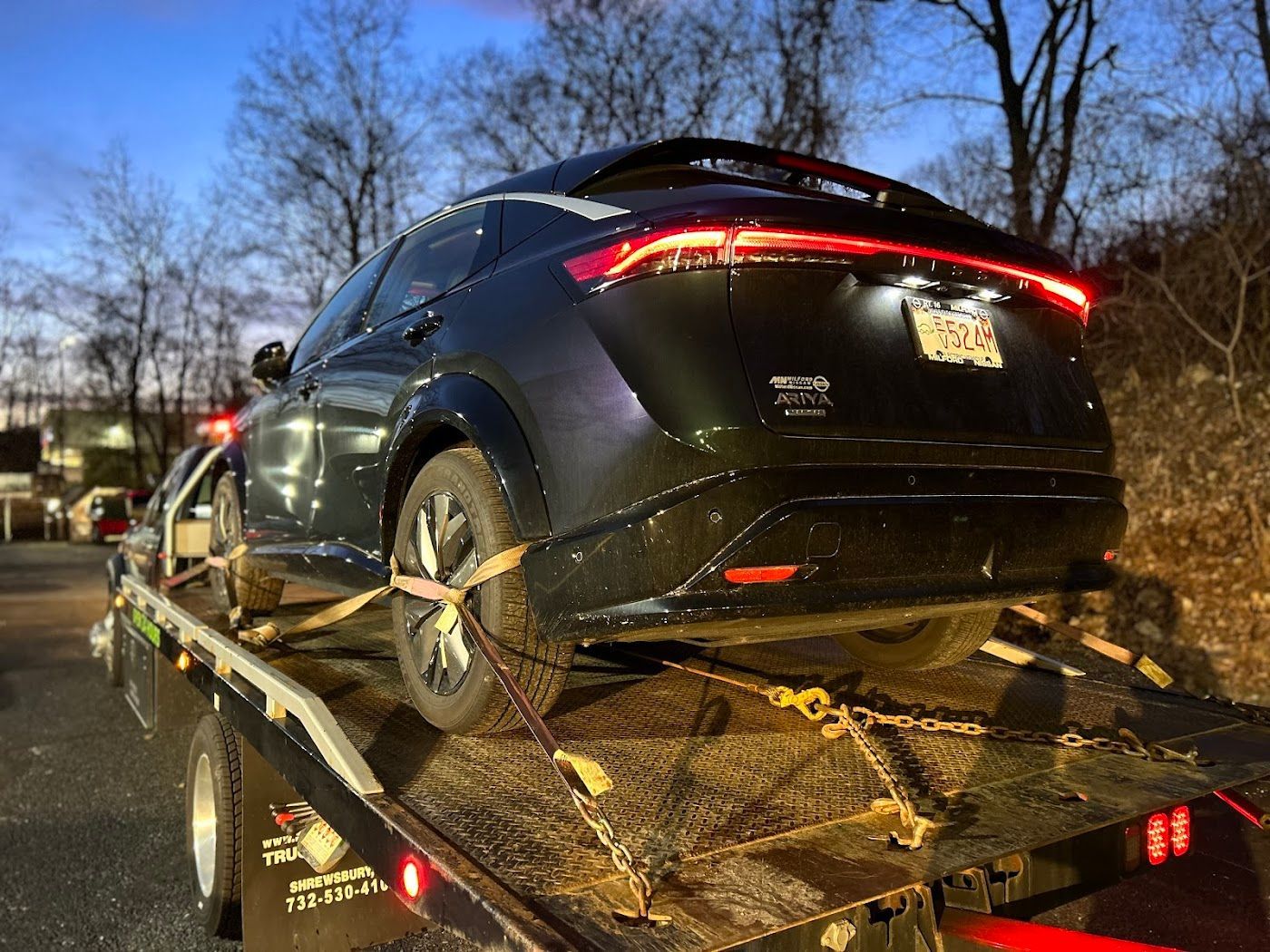 Black car secured on a tow truck, likely for transport, in an outdoor setting.