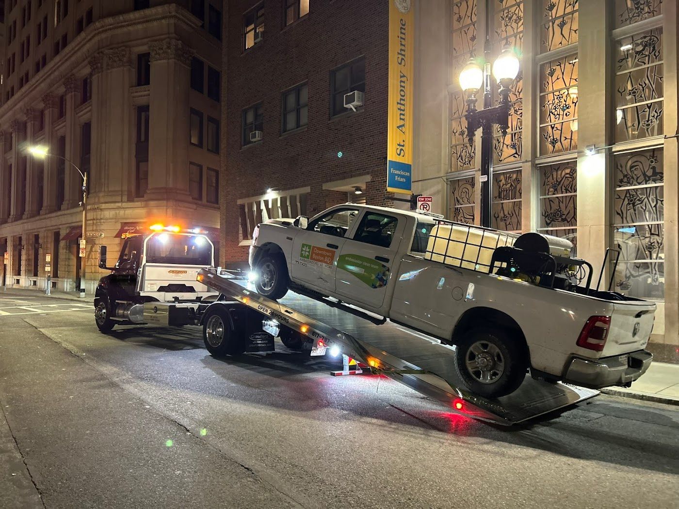 A white truck being towed onto a flatbed tow truck on a city street at night.