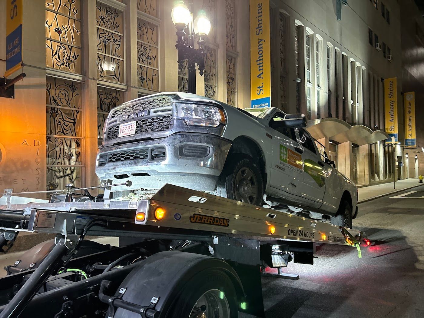 A damaged gray pickup truck is on a tow truck at night, in front of a building.