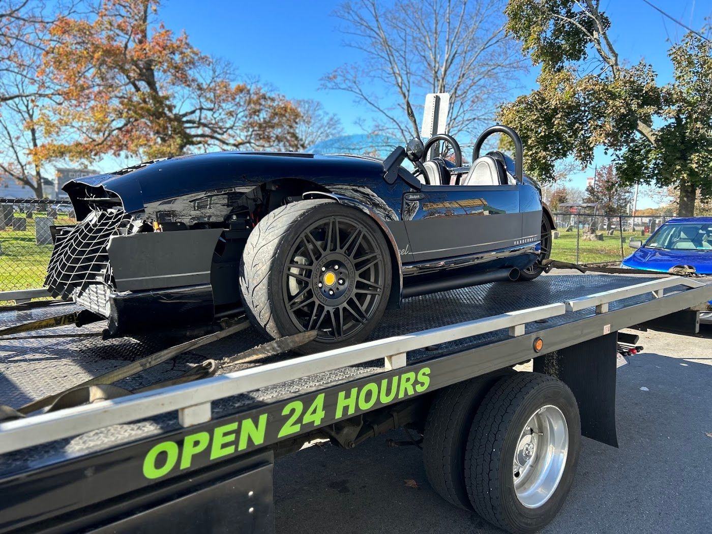 Black car with damage on a tow truck, roadside scene, blue sky.
