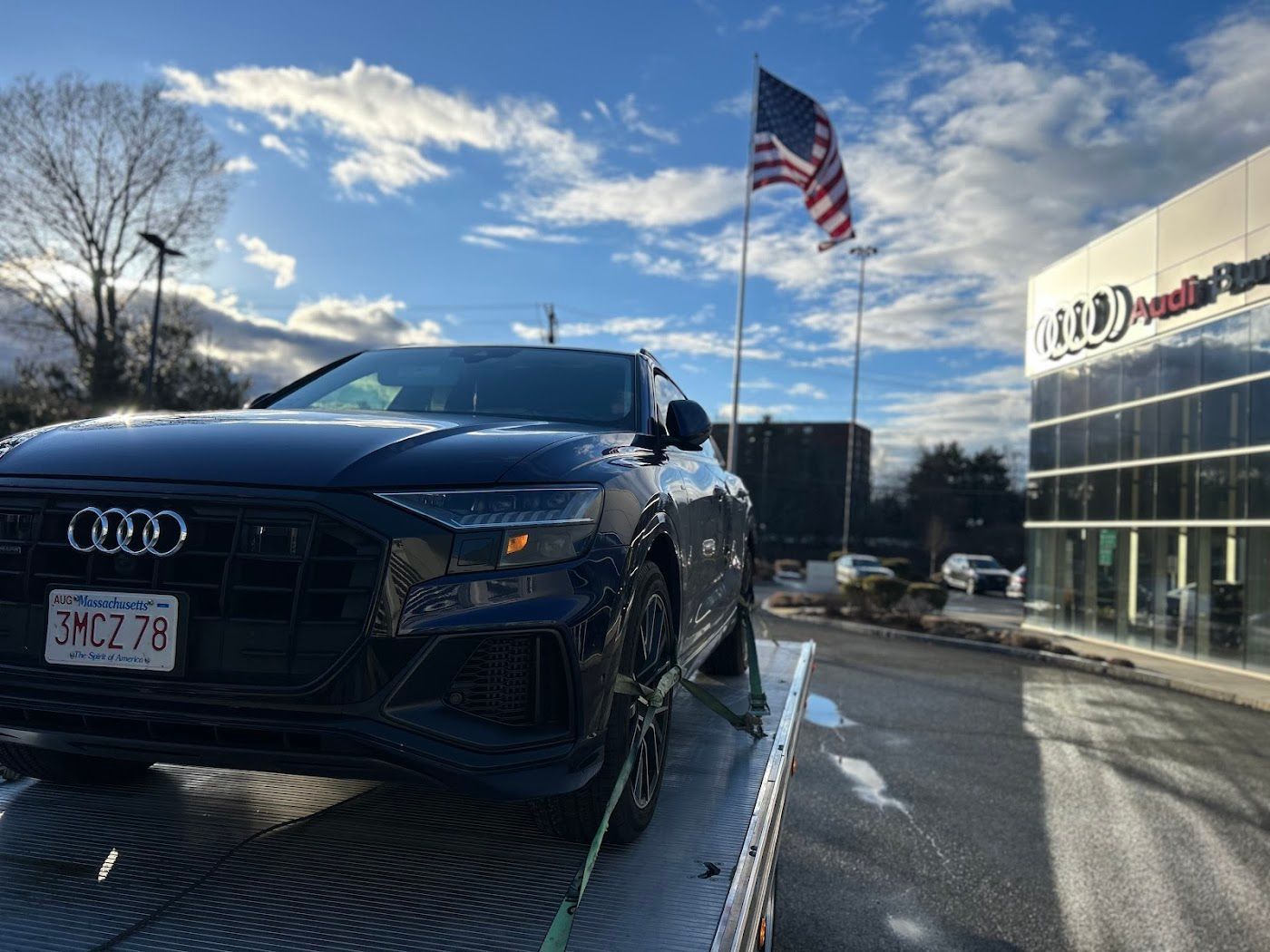 Black Audi SUV on a car hauler at an Audi dealership with the American flag in the background.