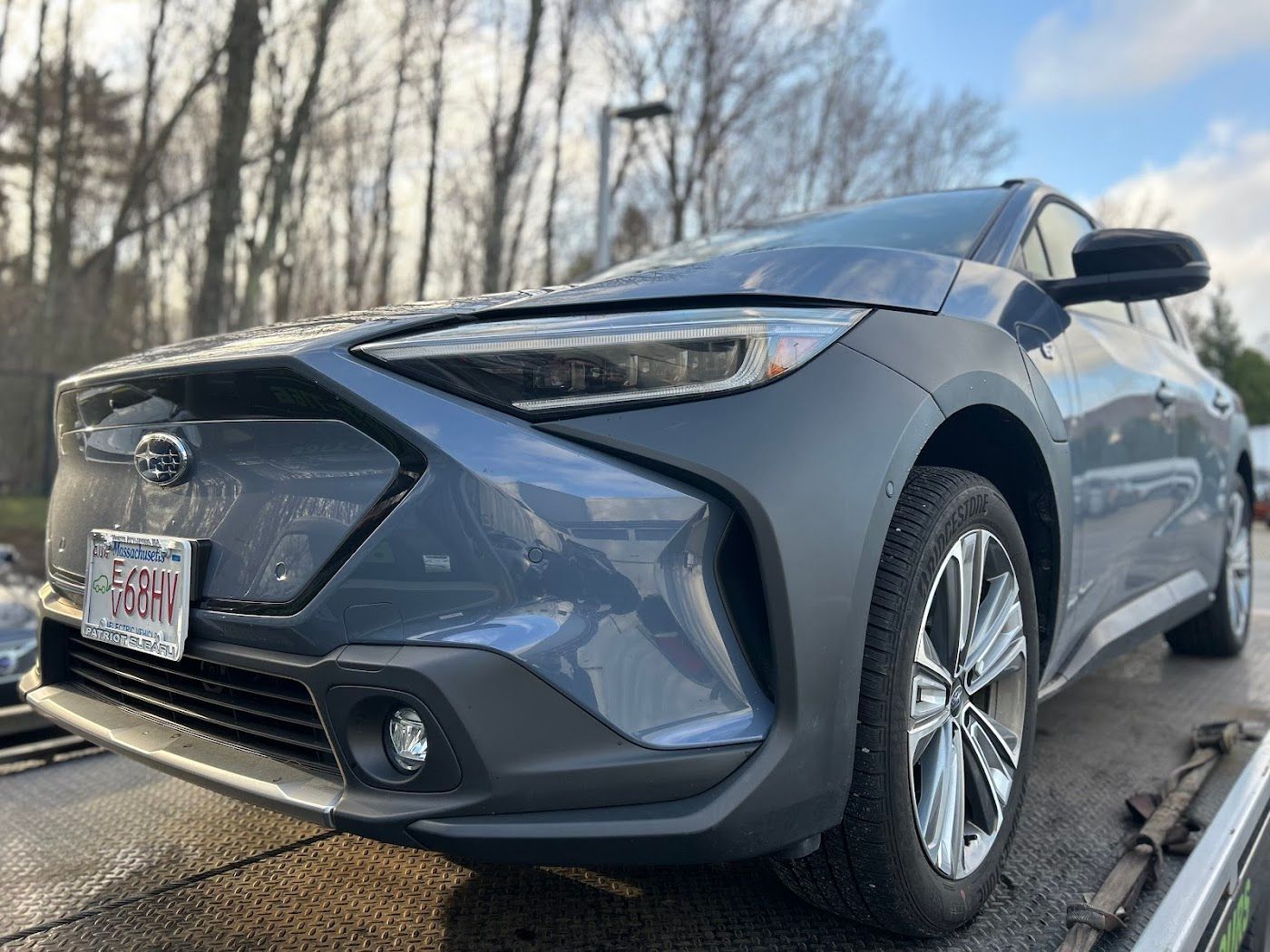 Blue Subaru Solterra EV on a tow truck, parked outside.