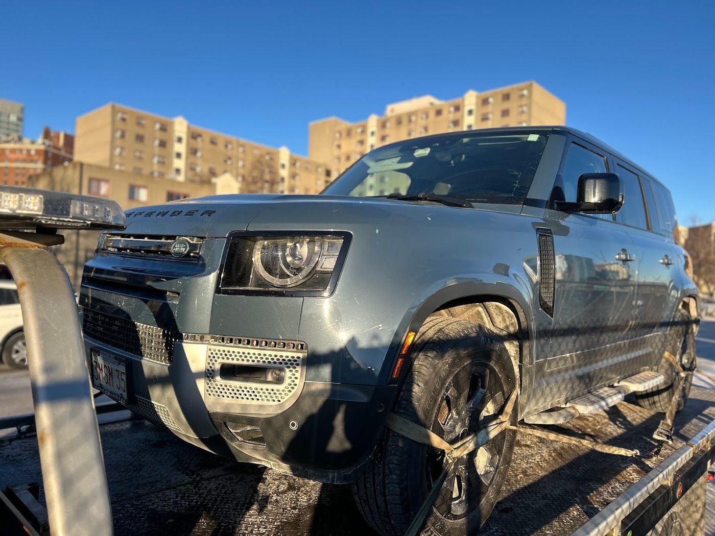 Blue Land Rover Defender SUV on a tow truck, snowy setting.