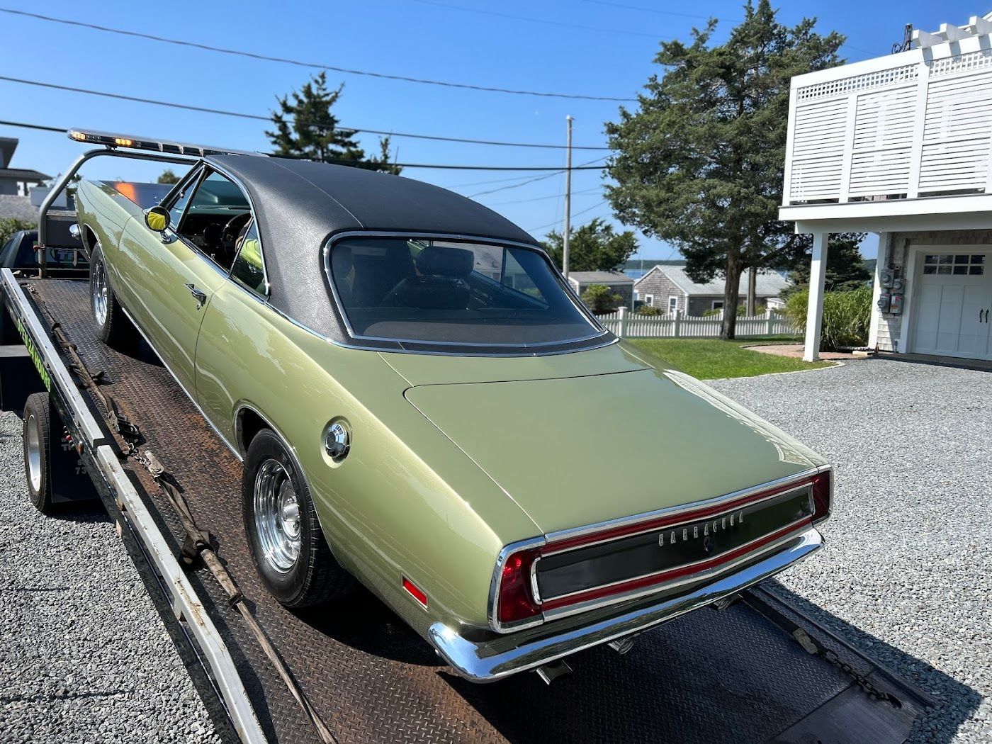 Green and black vintage car on a tow truck, parked on gravel driveway.