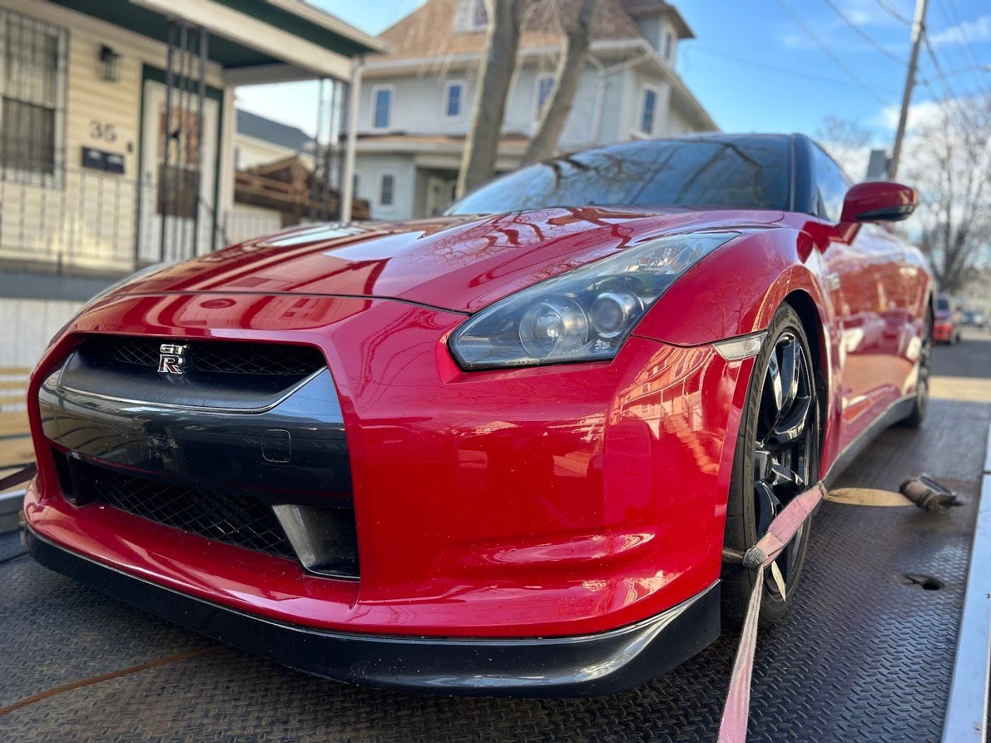 Red Nissan GT-R sports car secured to a flatbed tow truck in front of a residential house.