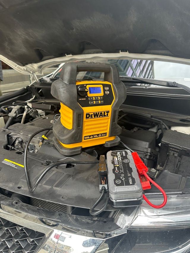 Yellow DeWalt jump starter on a car hood, jumper cables attached, ready to start a vehicle.
