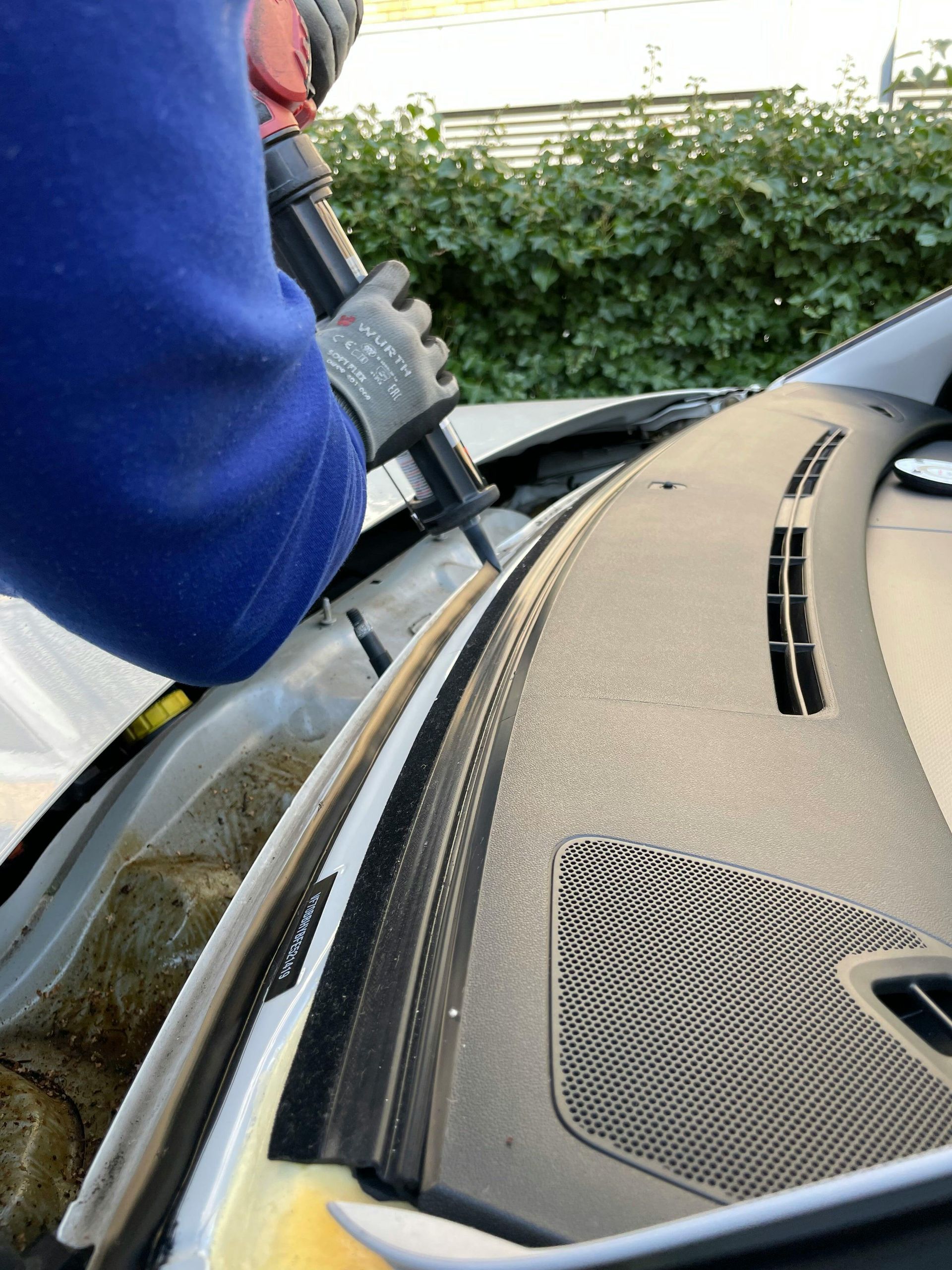 Person caulking the windshield frame of a silver car with a black caulk gun.