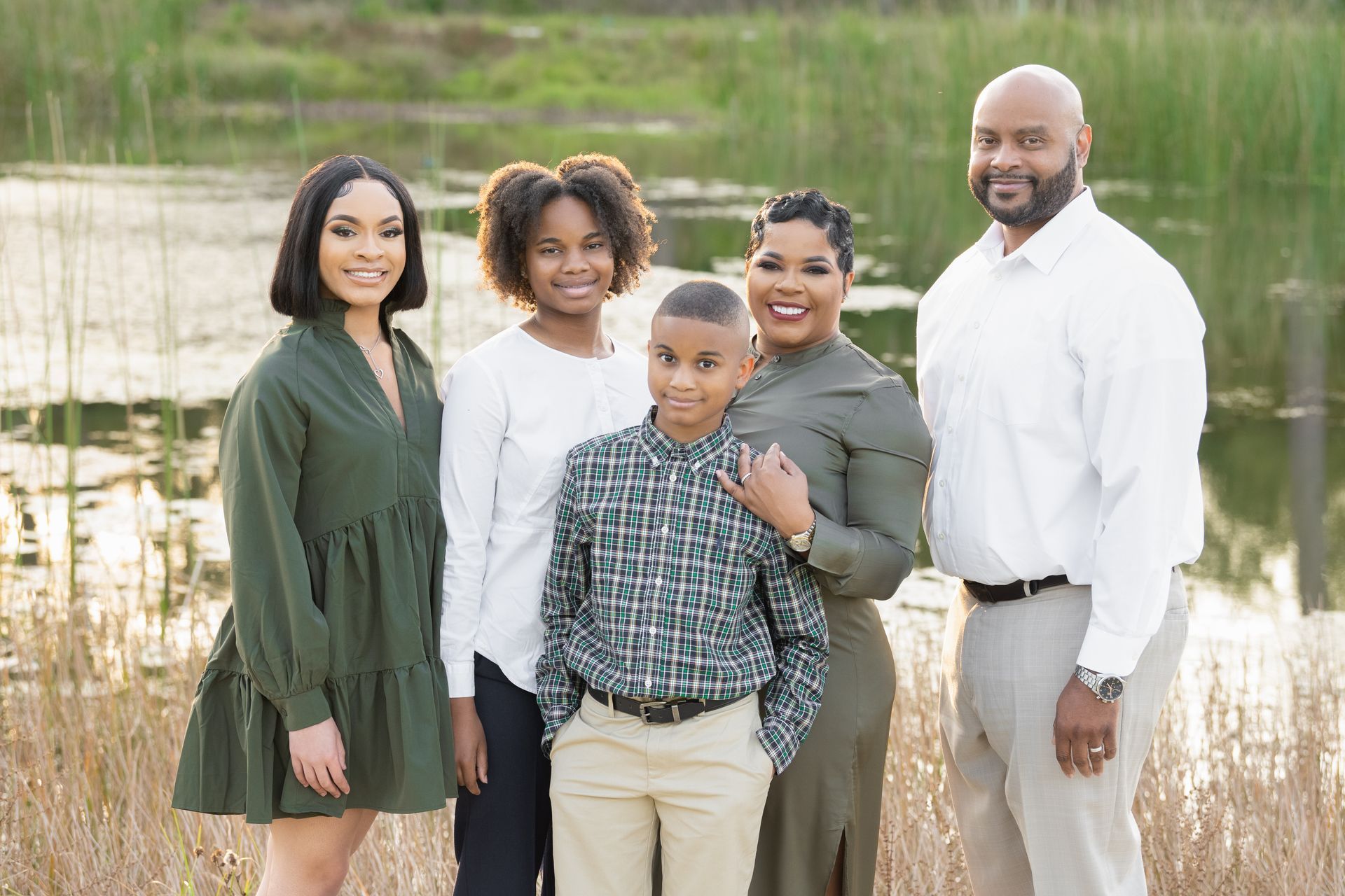 Family posing near a pond; woman in green dress, man in white shirt, children in neutral tones.