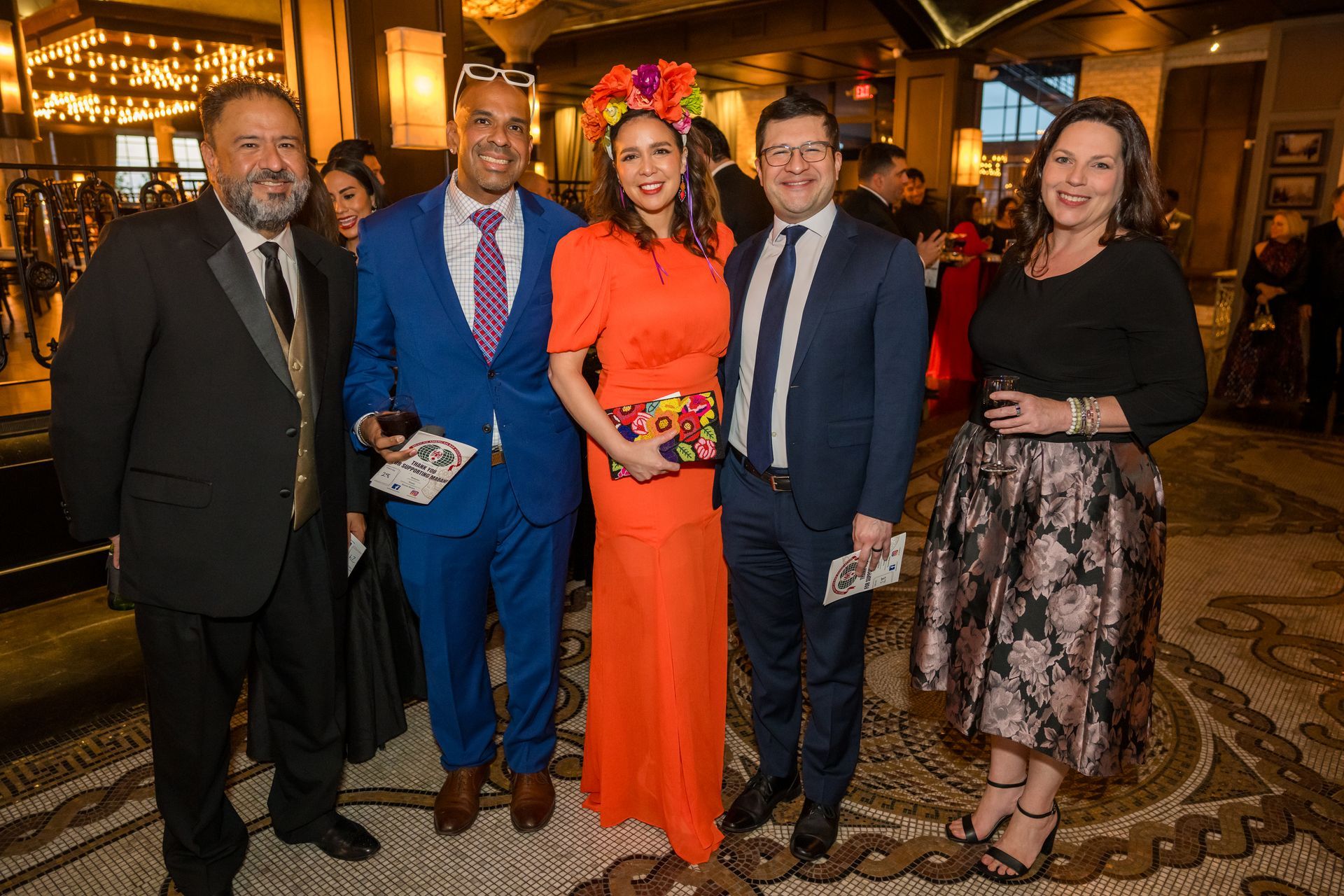 Group of five people posing for a photo at an event, mosaic tile floor, indoor setting.