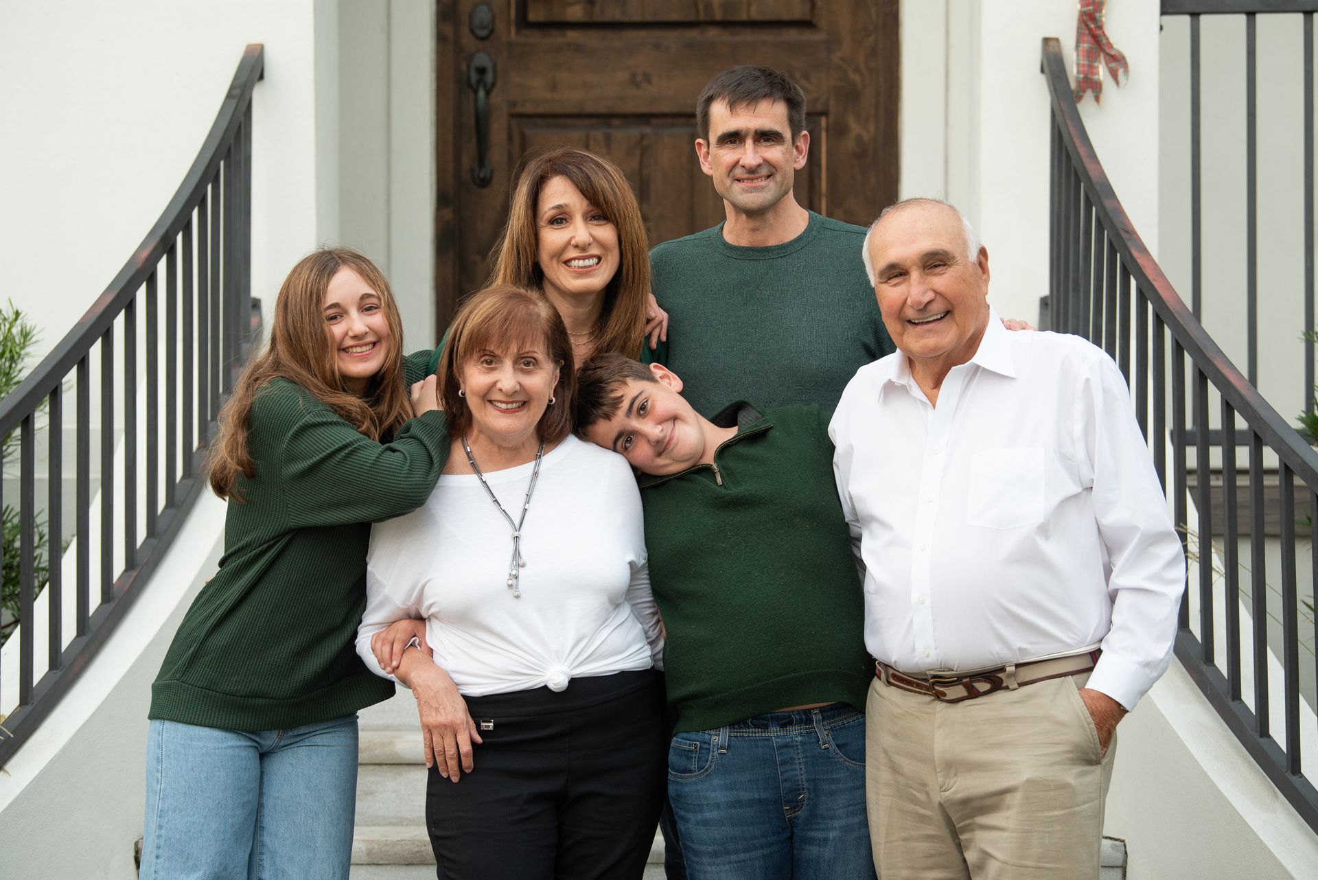Family portrait on front steps; two rows of people, smiling, wearing various green and white tops.