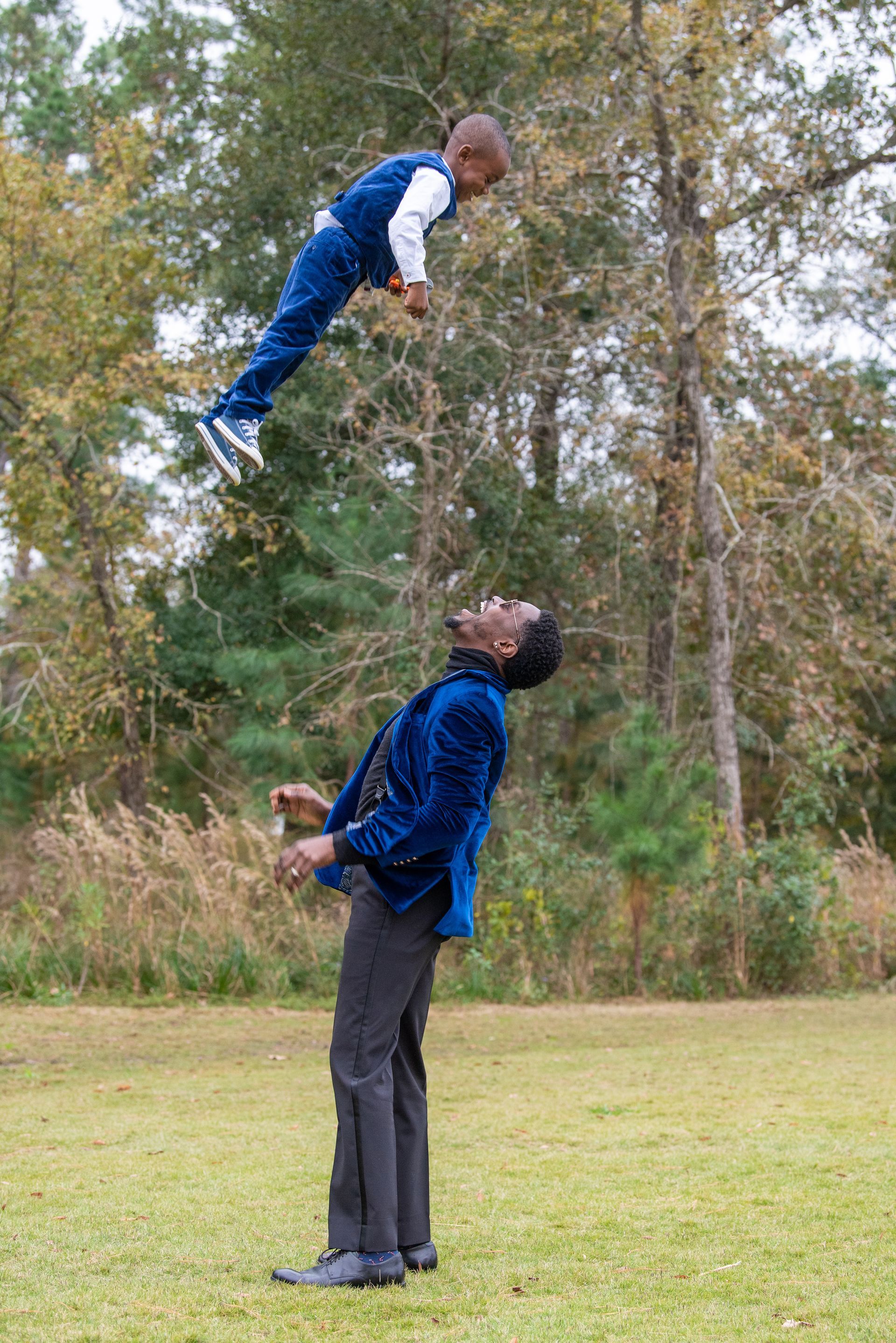 Man balancing child in air with head, outdoors.
