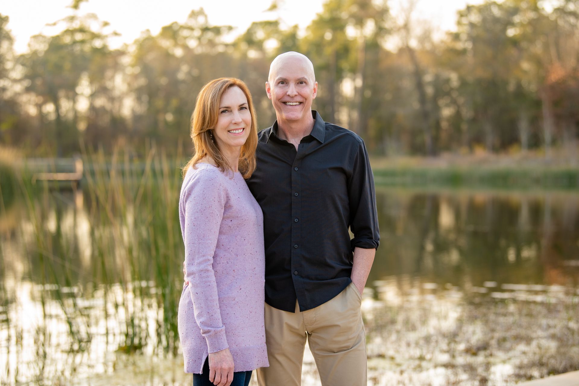 Couple standing near a lake, woman in a lavender sweater, man in black shirt.