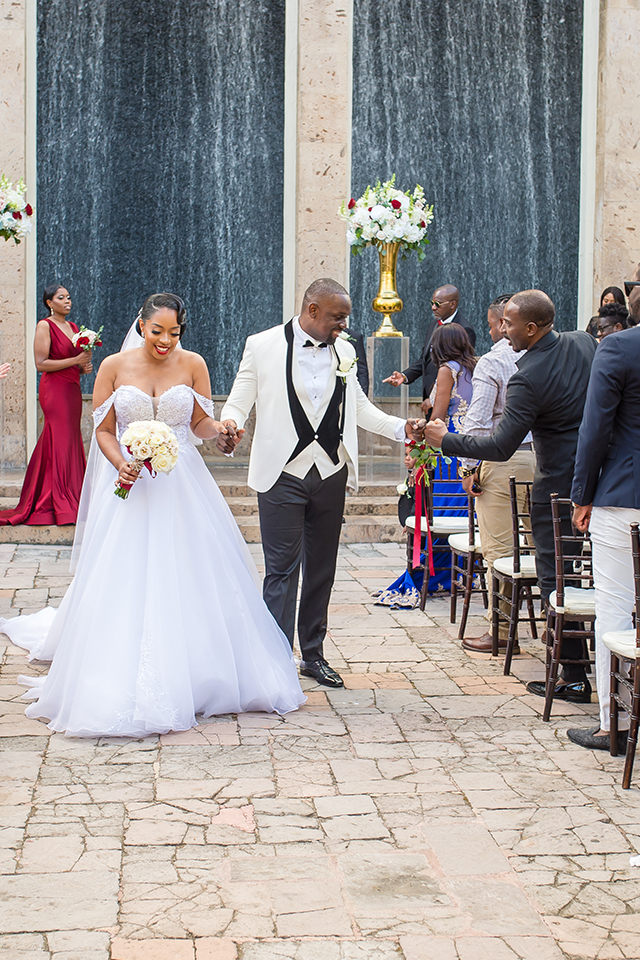 Bride and groom exiting wedding ceremony, holding hands, with waterfall backdrop.
