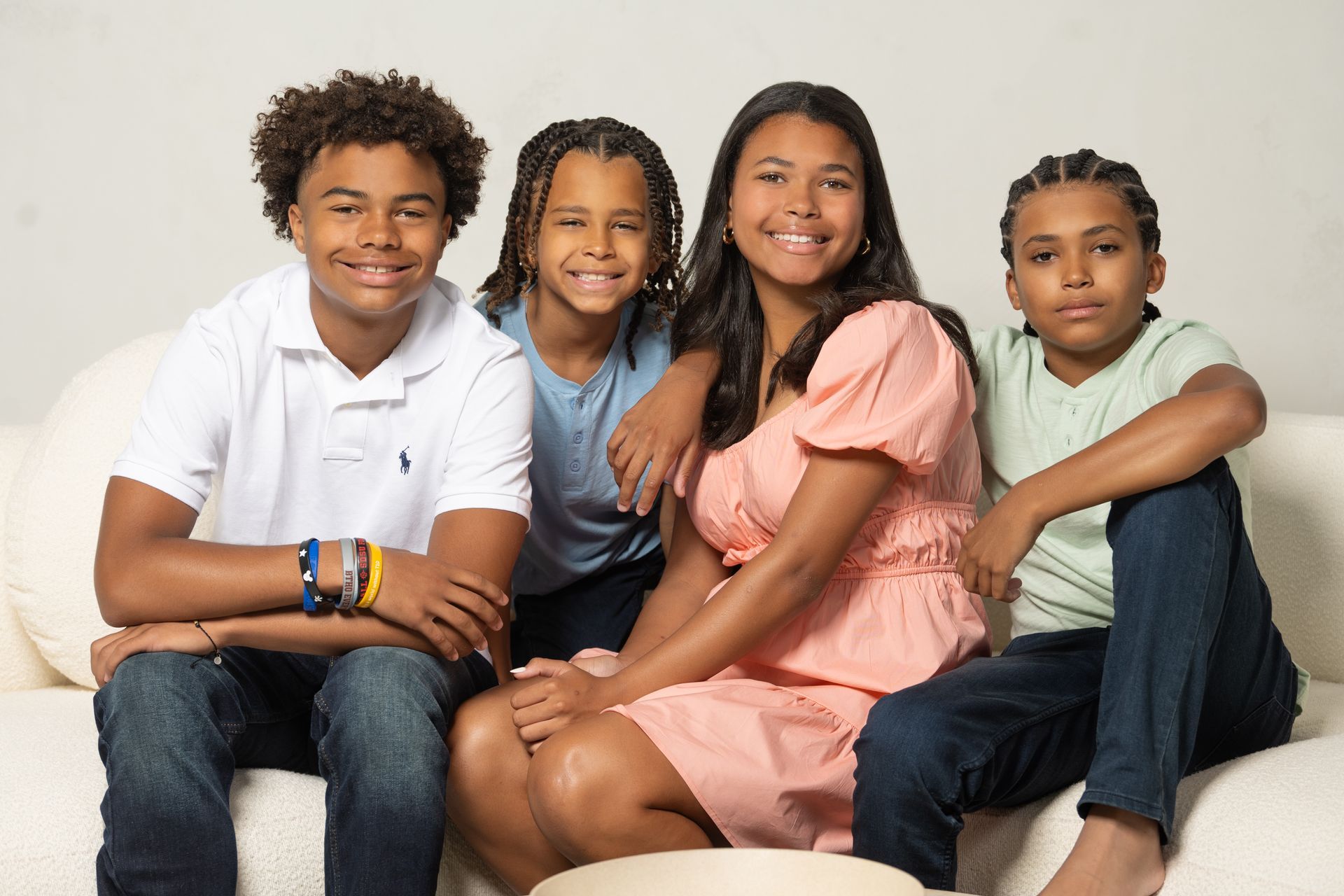 Four smiling people sit on a white couch. They appear to be posing for a photo.