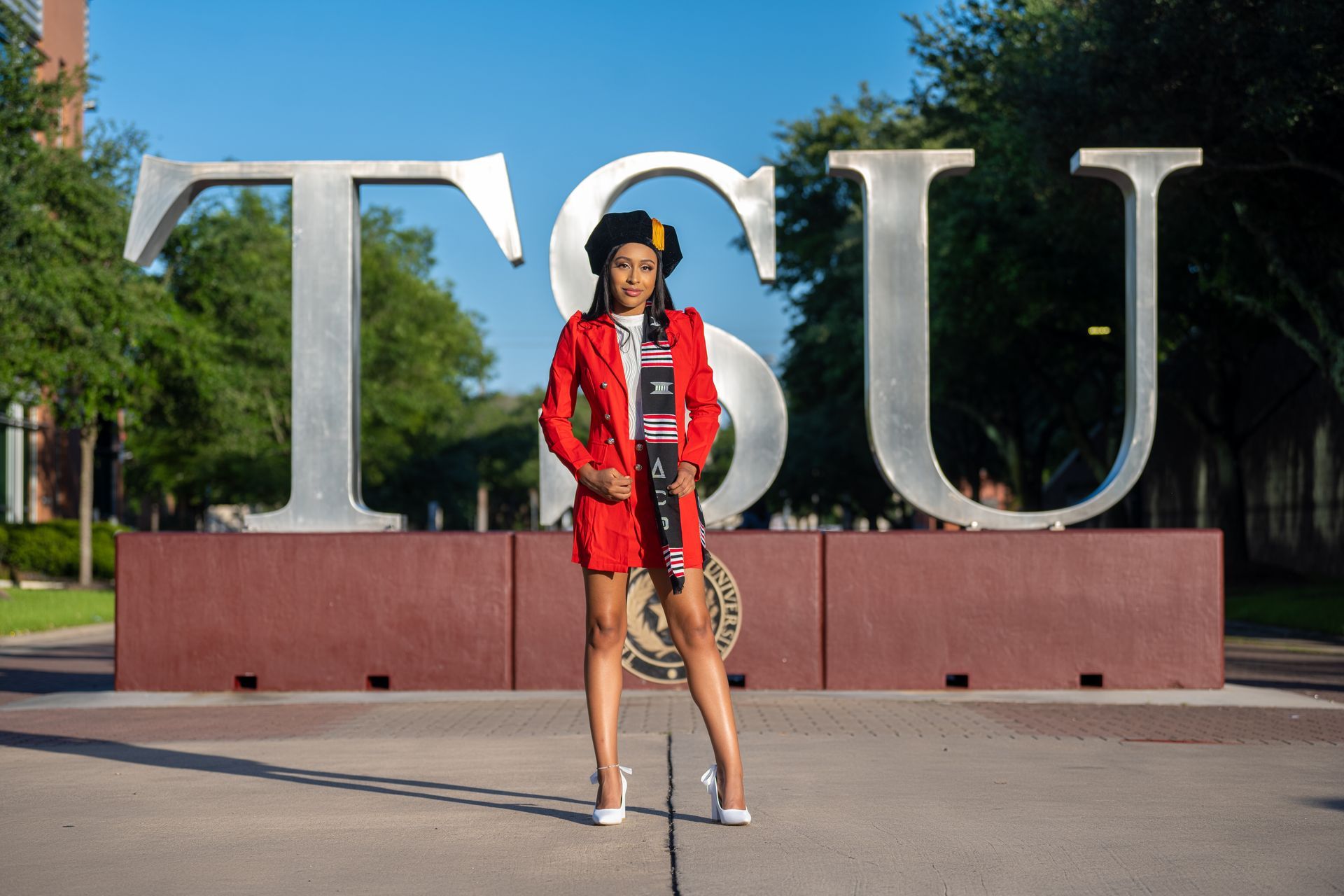 Woman in red blazer, cap, and sash stands in front of TSU letters.