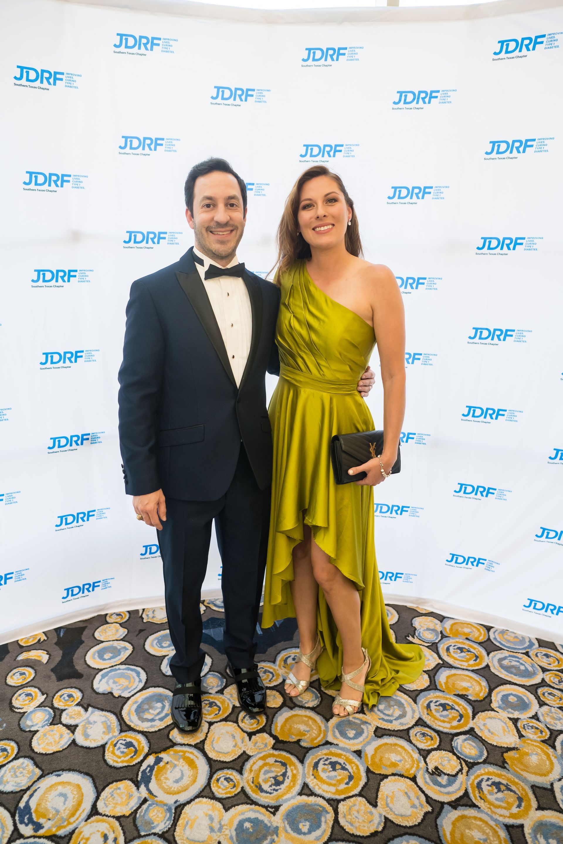 Man and woman pose at an event with a backdrop featuring the JDRF logo.