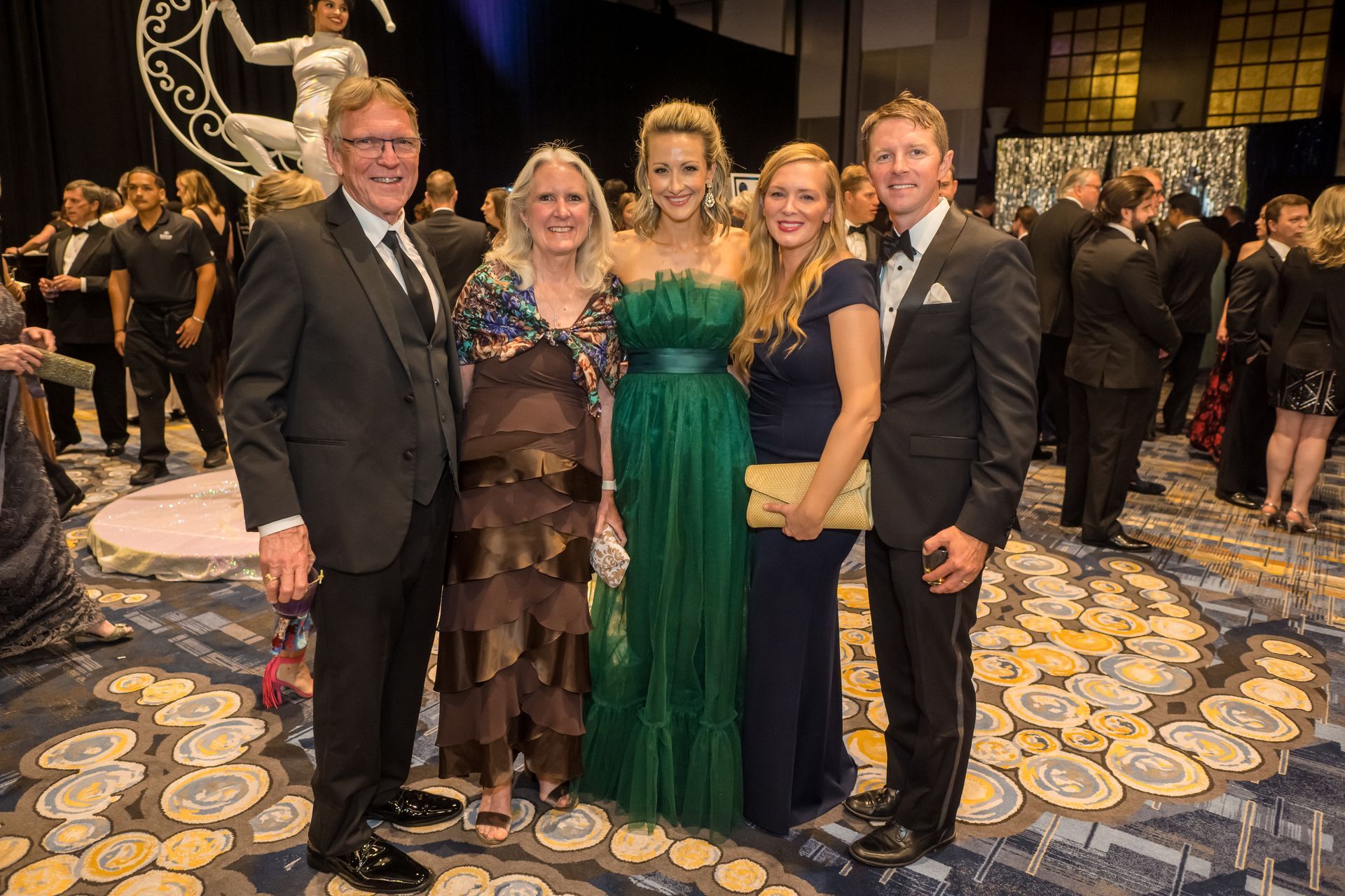 Five people in formal attire at an event, with a large decorative backdrop.