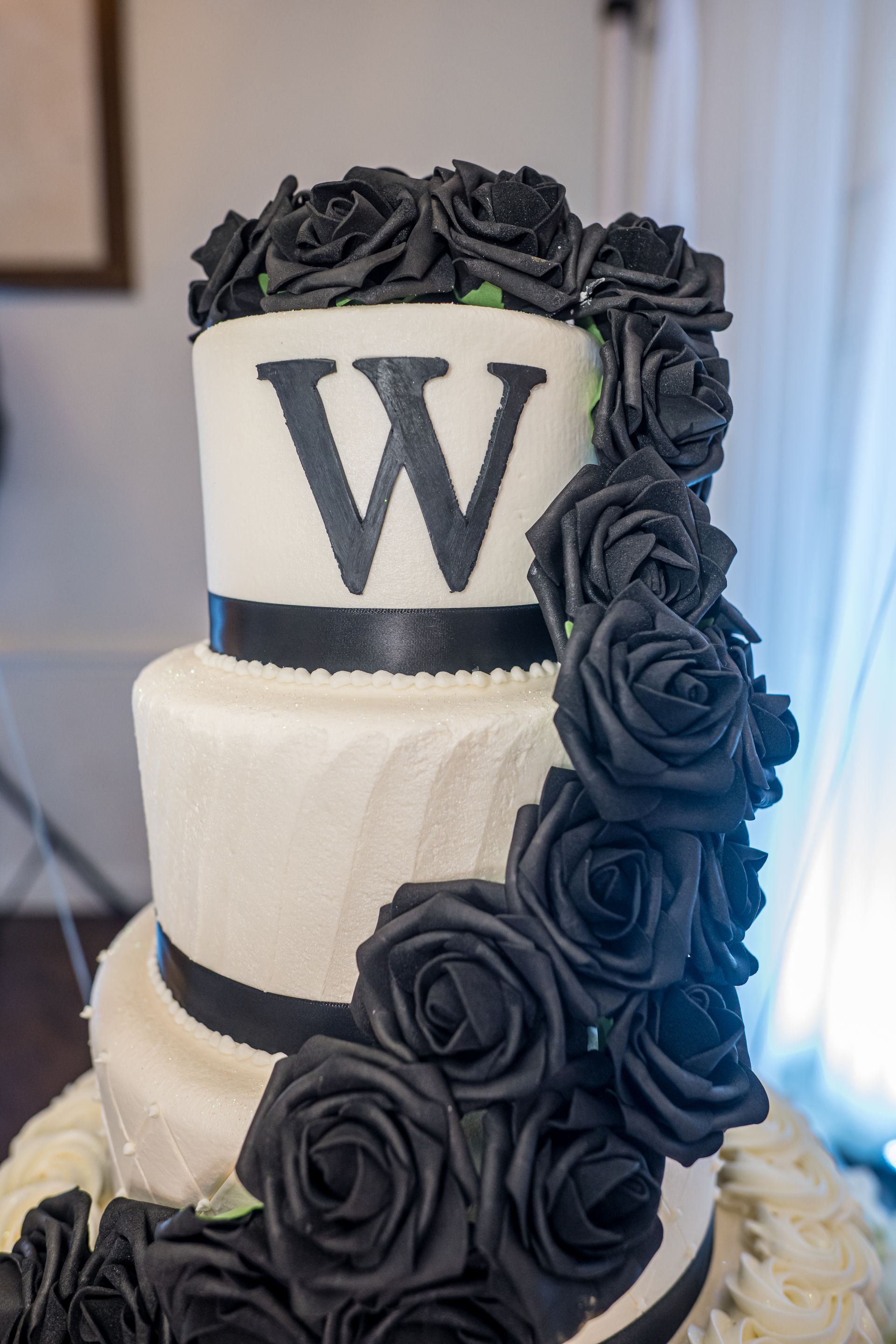 Three-tiered white cake with black roses cascading down and