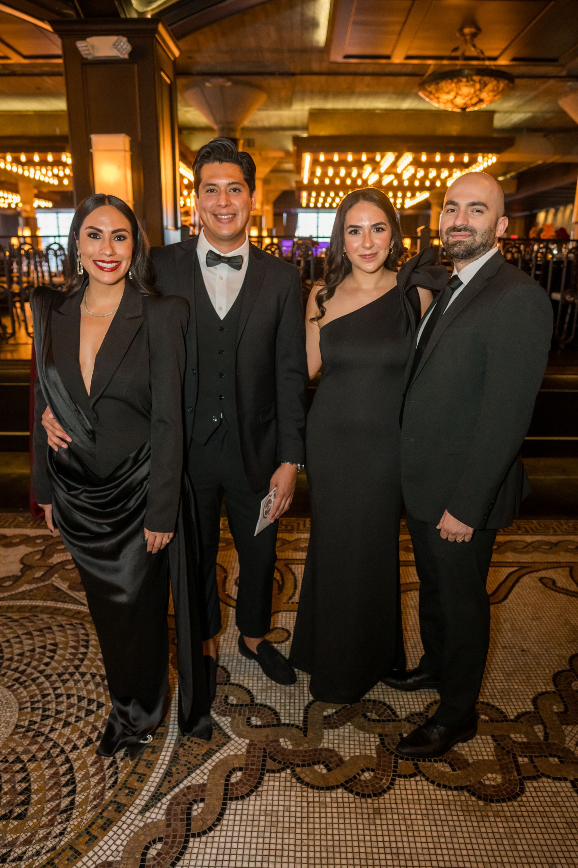 Four people posing formally in a luxurious setting. Two women and two men in black attire, smiling.