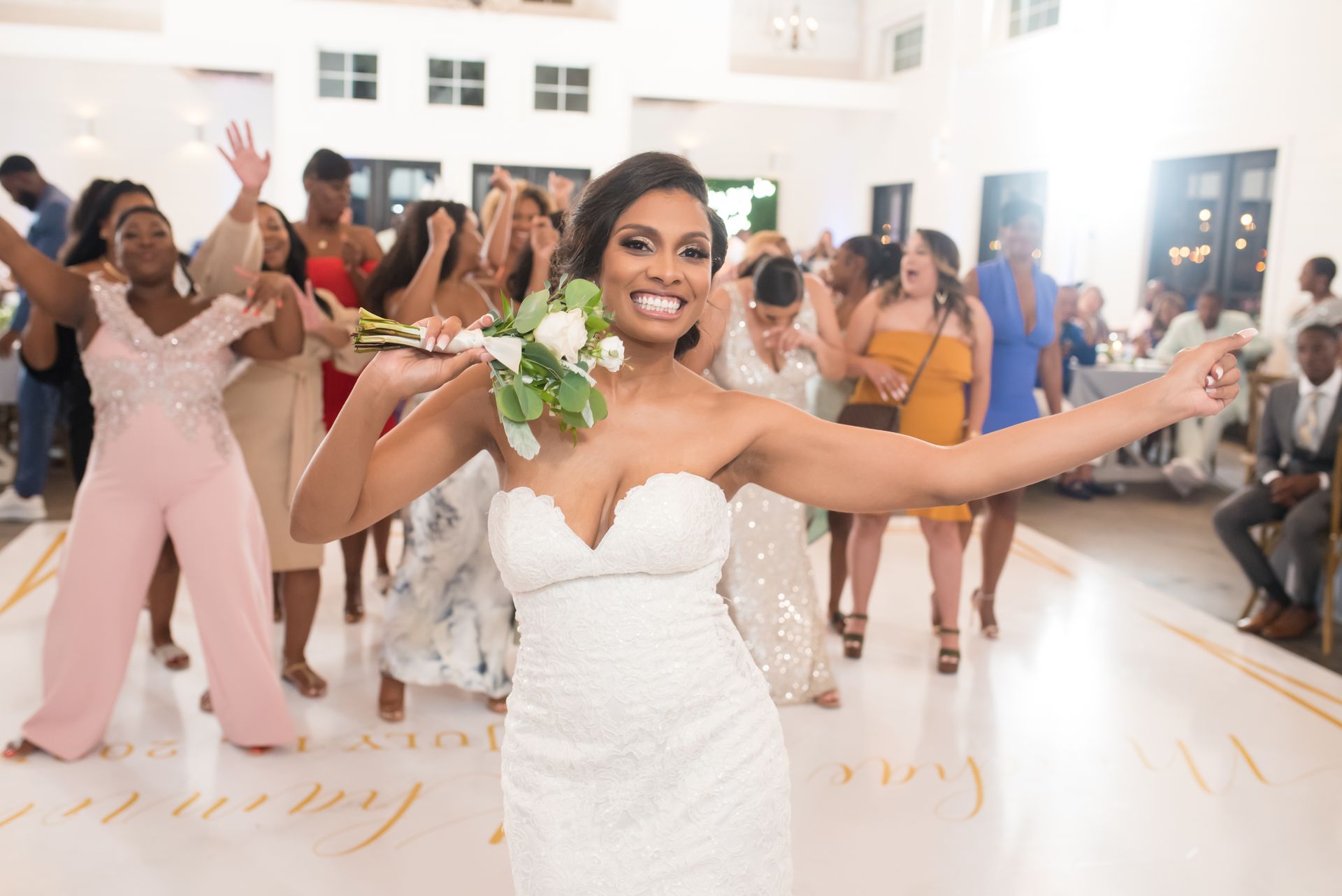 Bride throws bouquet, celebrating with bridesmaids in a ballroom.