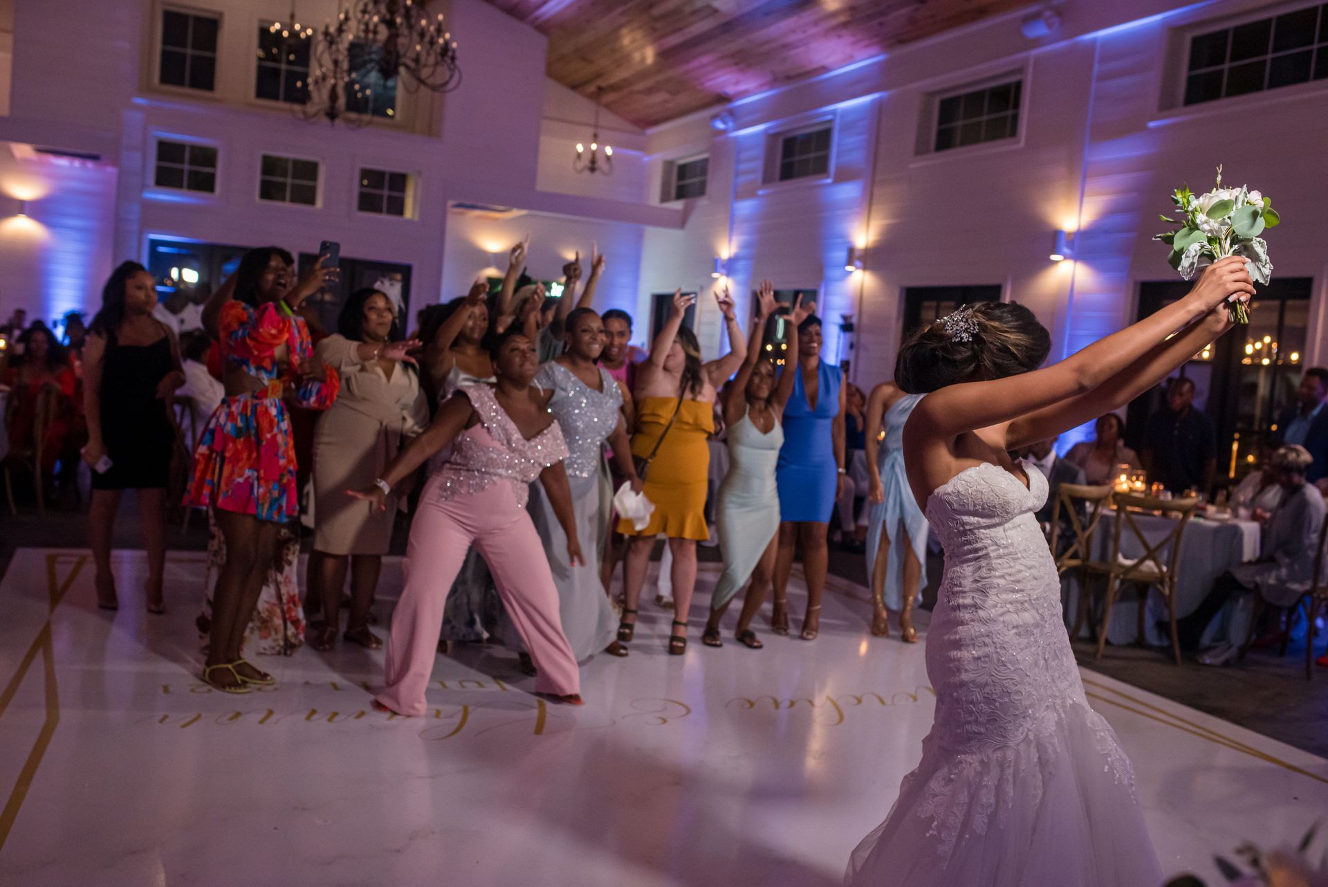 Bride throwing bouquet at a wedding reception. Guests reaching up, white and gold dance floor, soft lighting.
