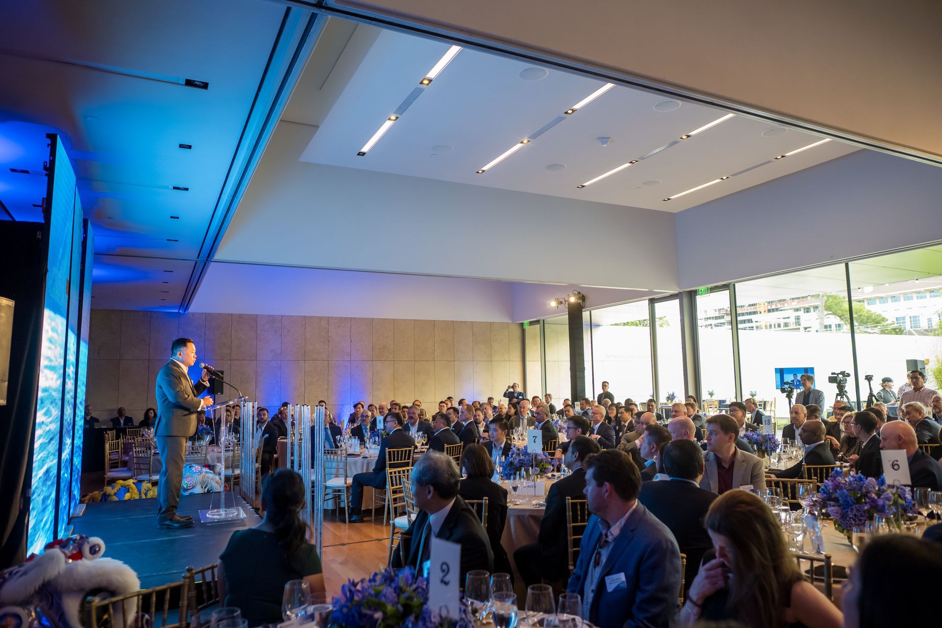 Man speaking on stage at event, addressing seated audience in a bright, modern room.