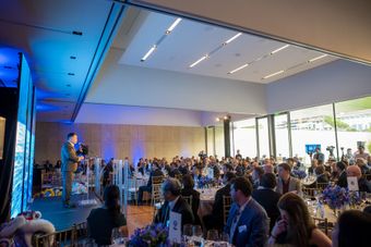 Man speaking on stage at event, addressing seated audience in a bright, modern room.