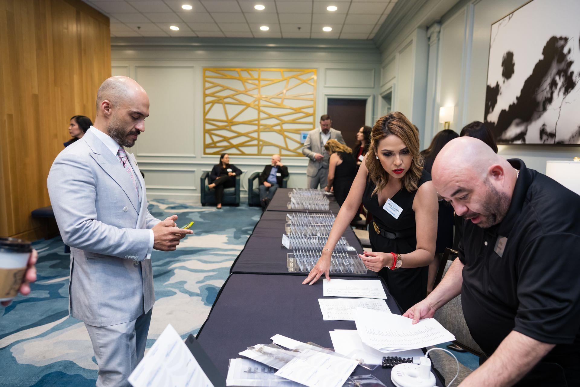 People at a registration table in a brightly lit room. A man looks on while two people work on paperwork.