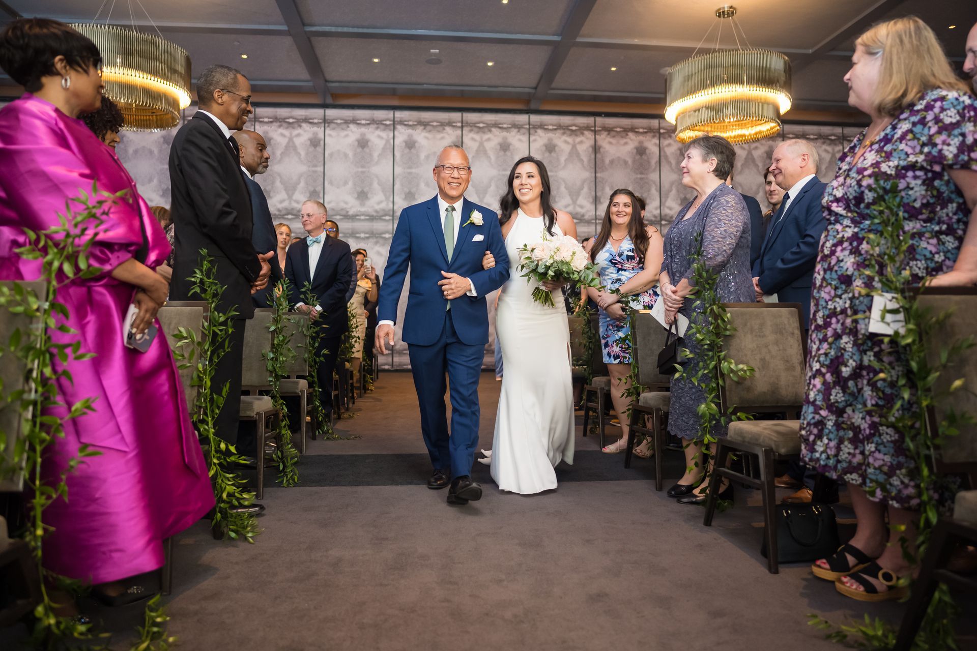 Bride walks down the aisle with her father at a wedding ceremony; guests watch.