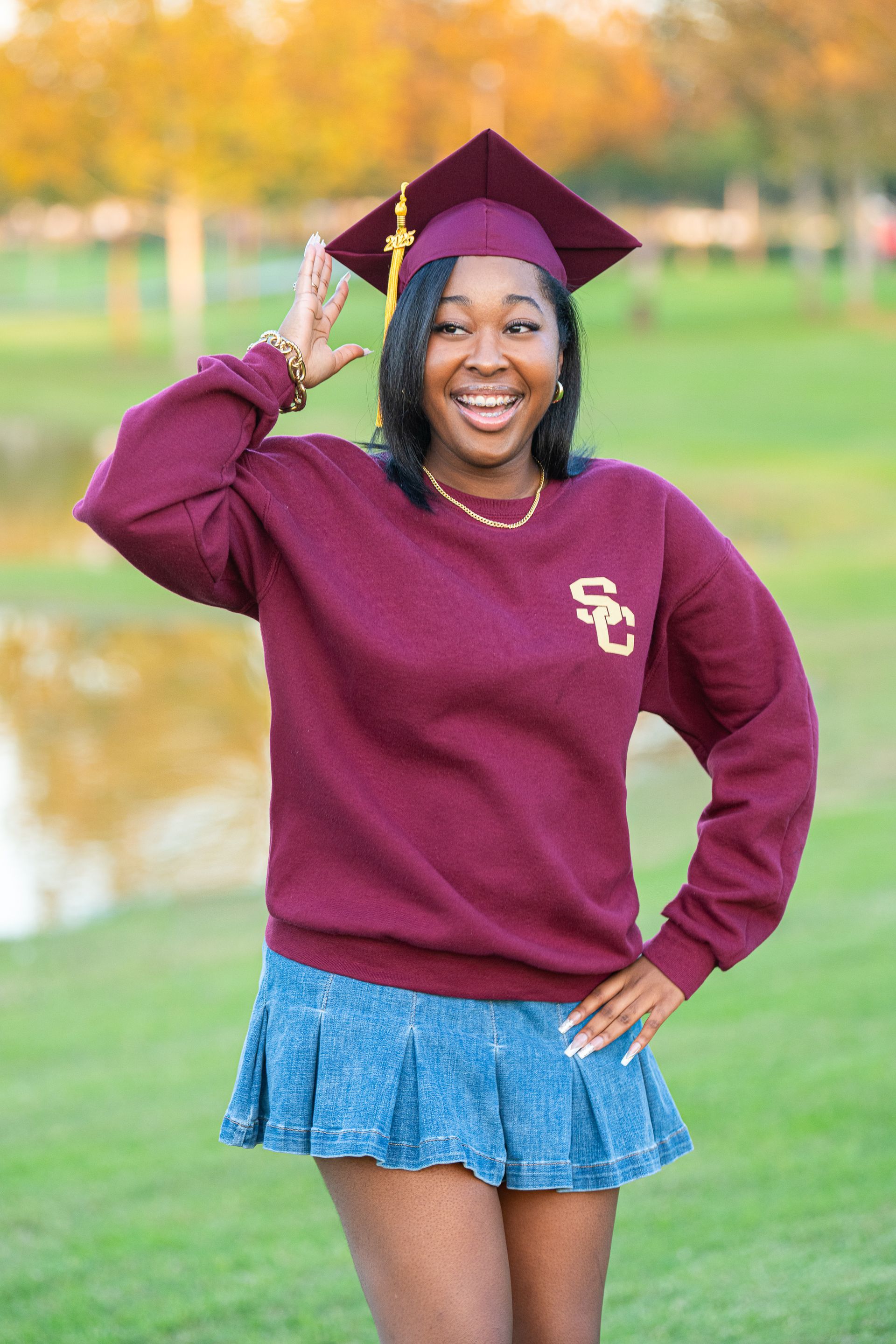 Woman in maroon sweatshirt and graduation cap, smiling and posing outdoors.