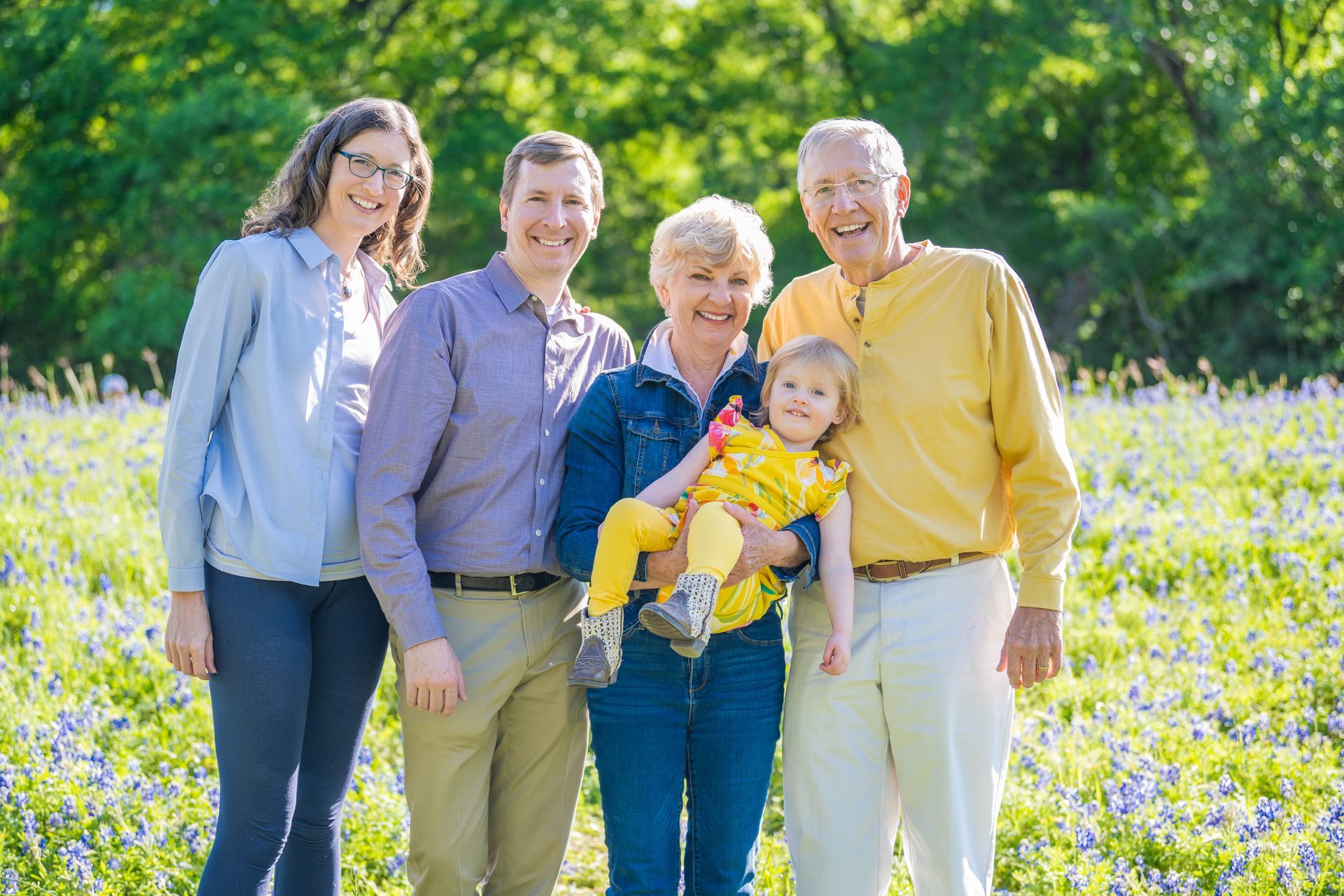 Family posing outdoors among blue wildflowers. Cheerful smiles, casual attire.