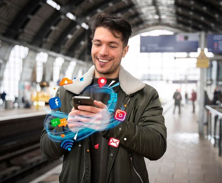 Smiling man using phone at train station, surrounded by social media icons.
