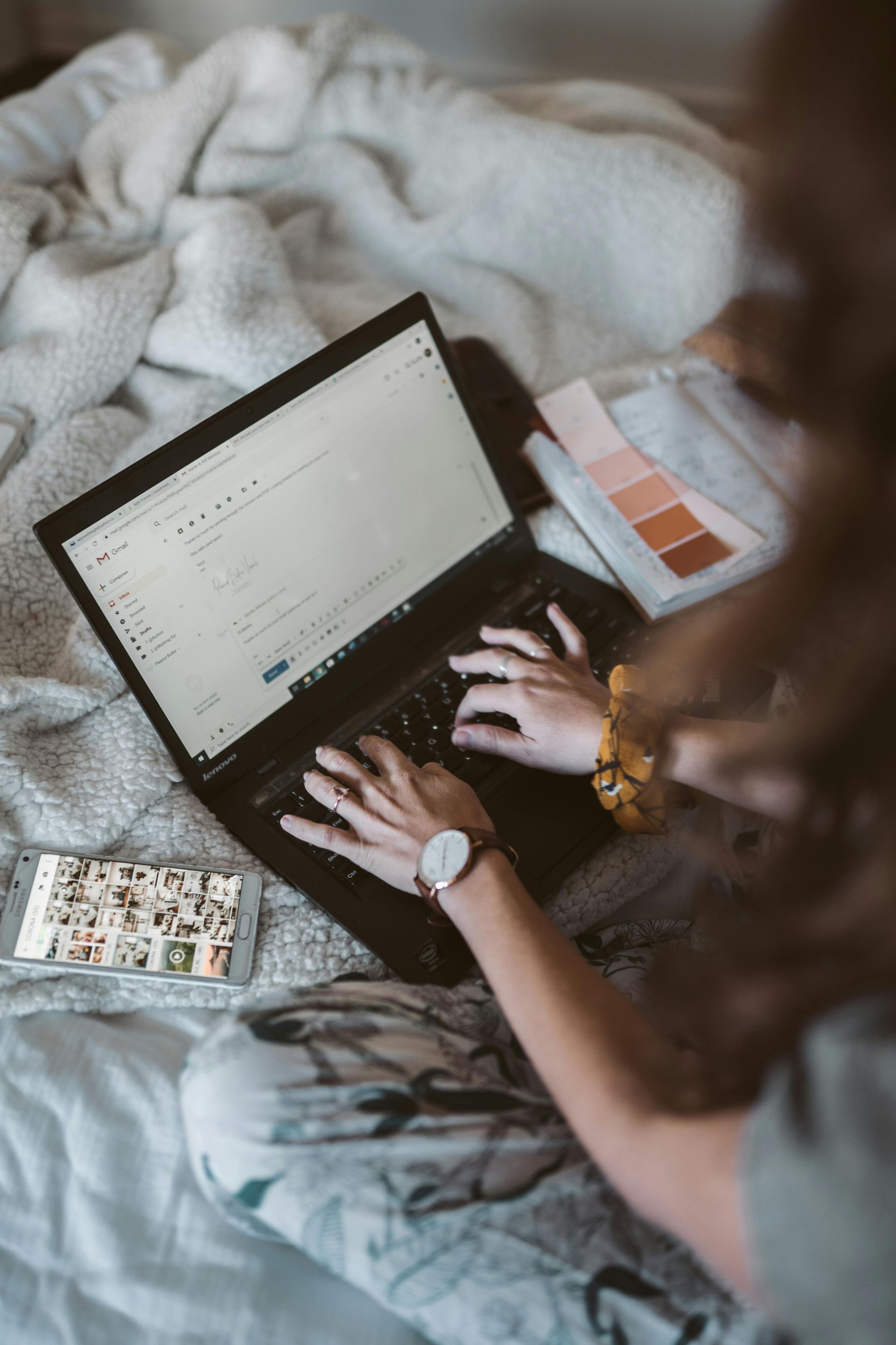 Woman working on laptop in bed; phone nearby; color swatches.
